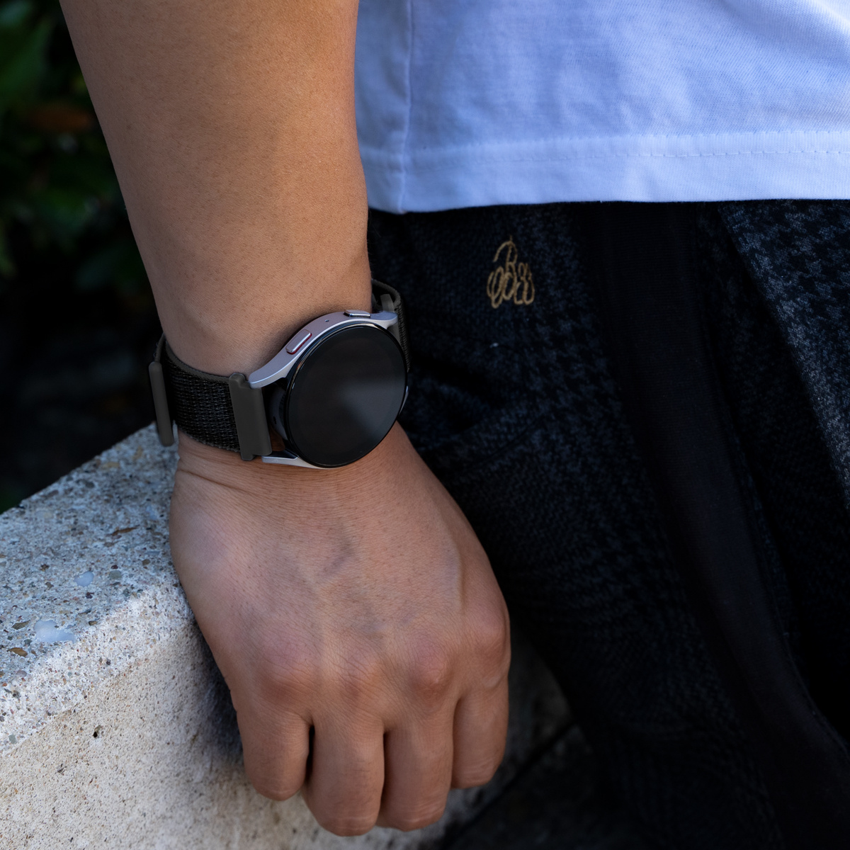Handgelenk mit Smartwatch, schwarzer Bildschirm und schwarzes Stoffarmband.