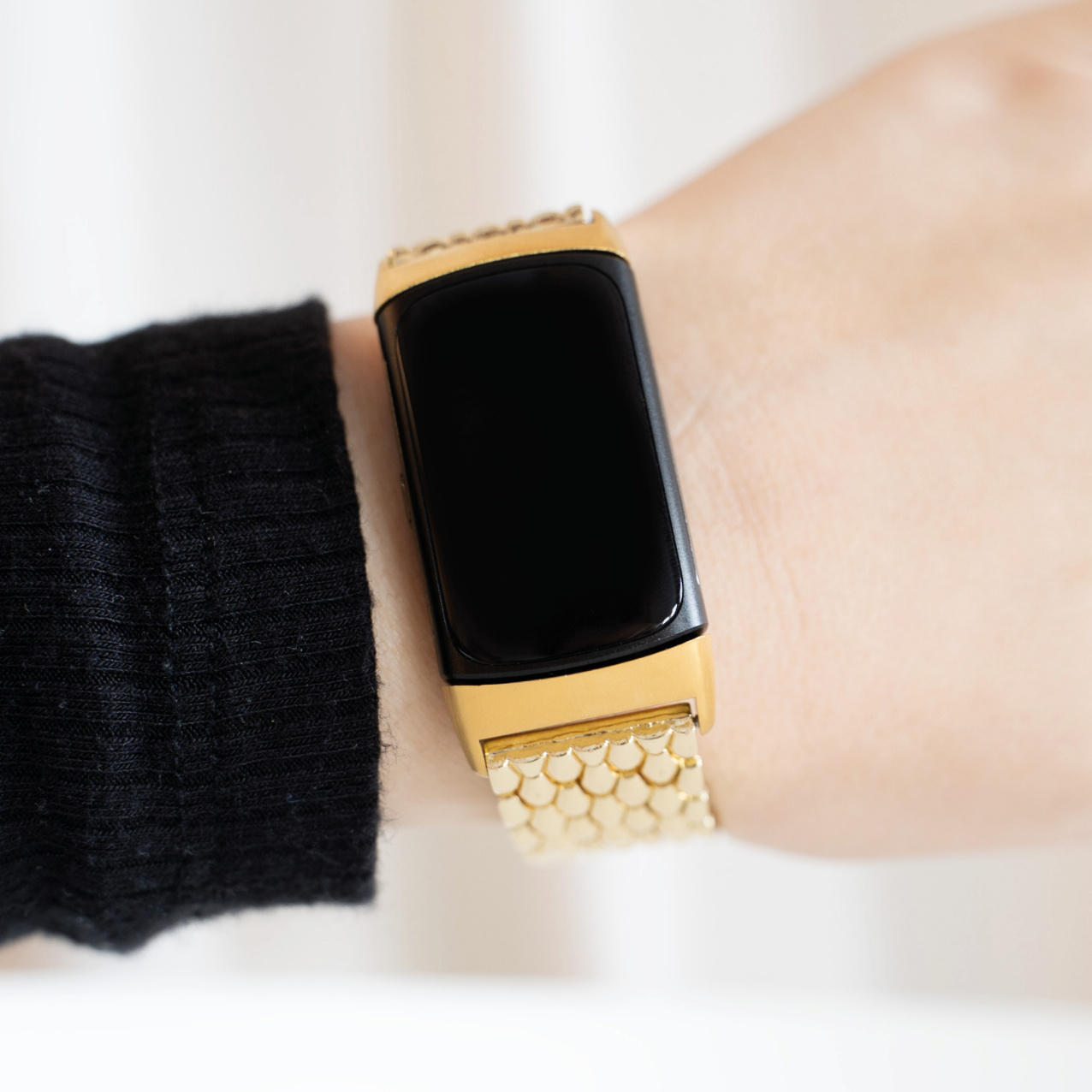 Goldener Fitness-Tracker im Armbandstil am Handgelenk. Schwarzer Bildschirm. Weißer Hintergrund.