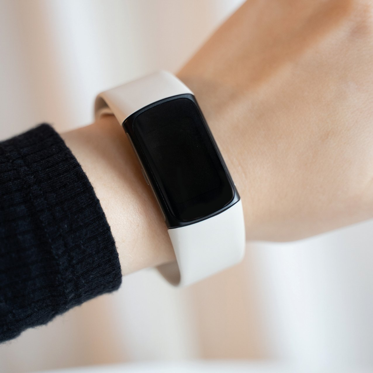 Das Handgelenk einer Person, die eine cremefarbene Smartwatch mit schwarzem Bildschirm trägt.