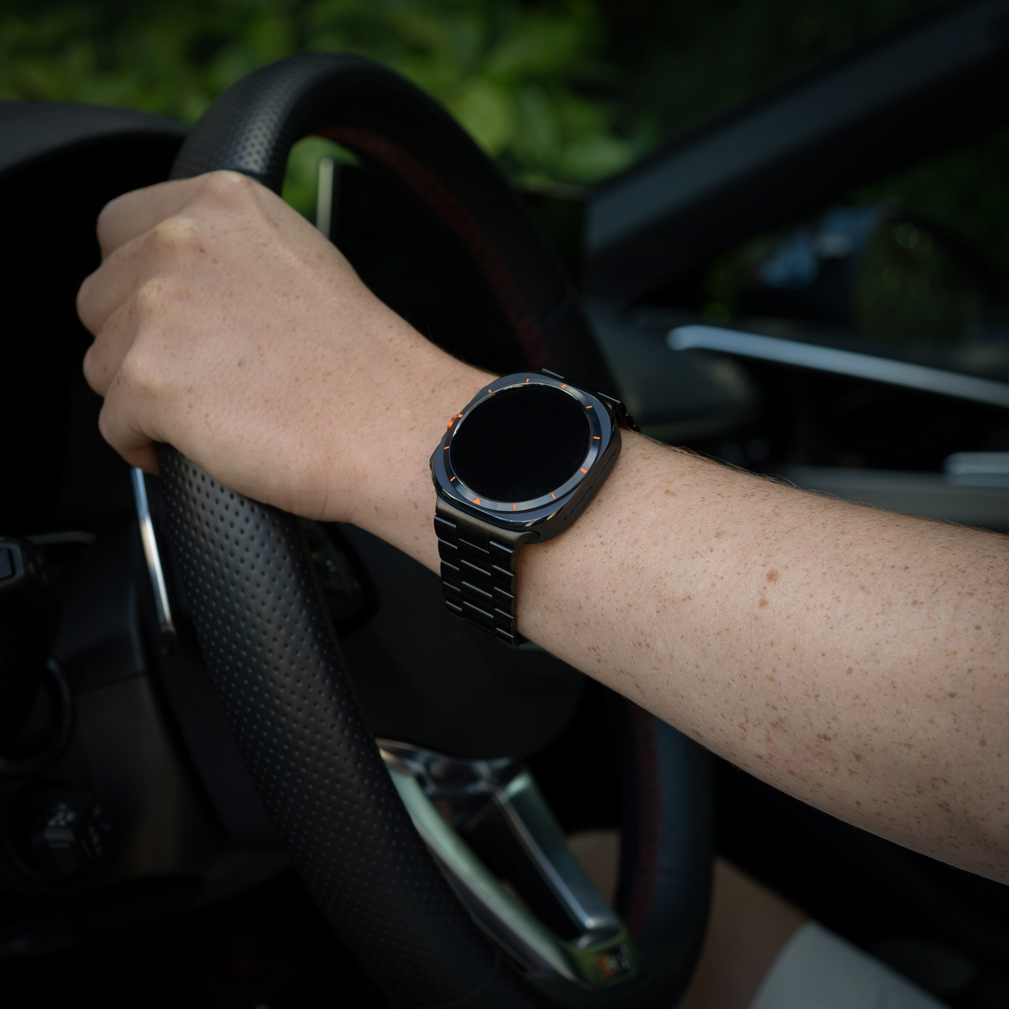 Eine Person mit schwarzer Uhr hält ein Lenkrad. Die Uhr ist am Handgelenk.