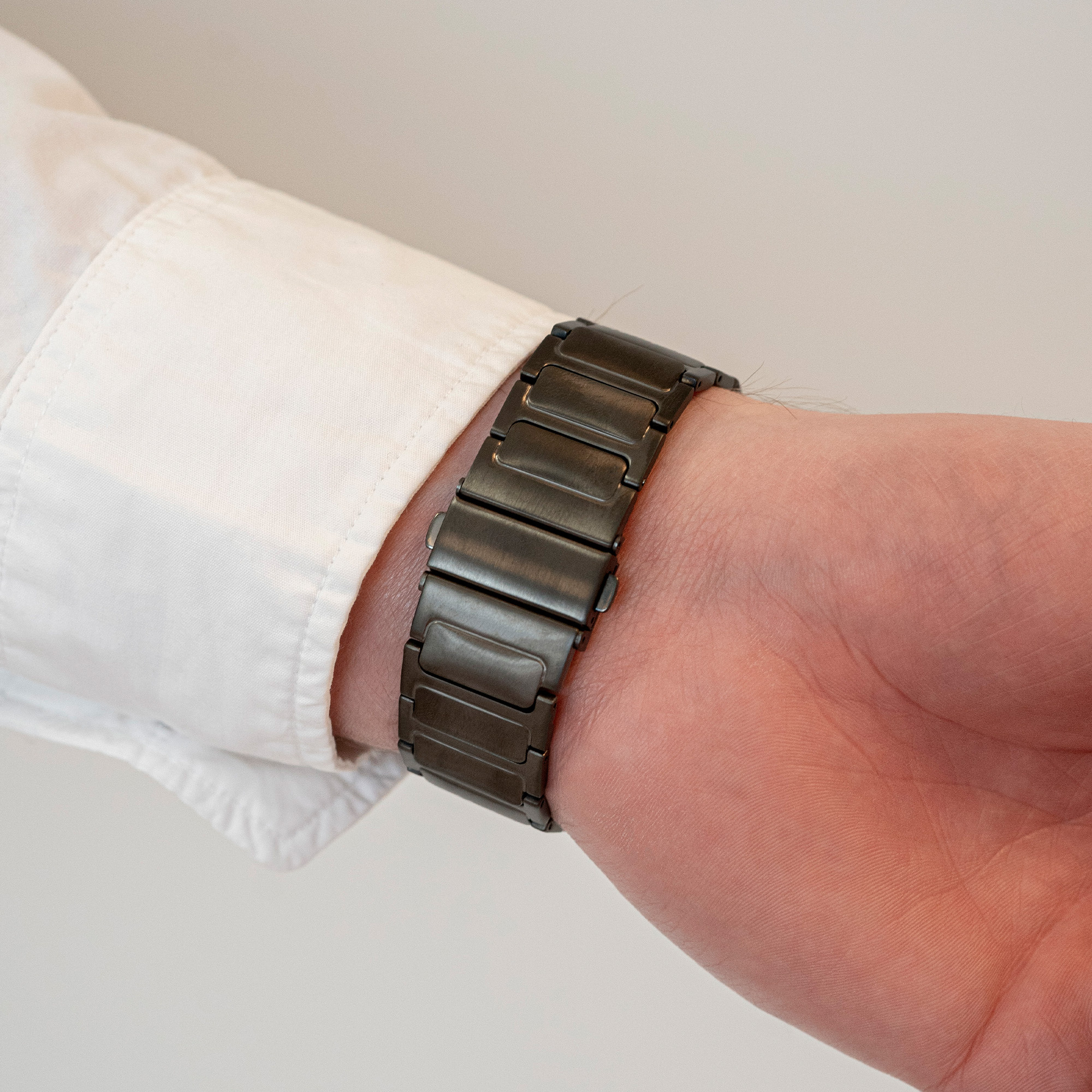 Handgelenk mit dunklem Metall-Uhrenarmband. Das Band besteht aus verbundenen Metallplatten.