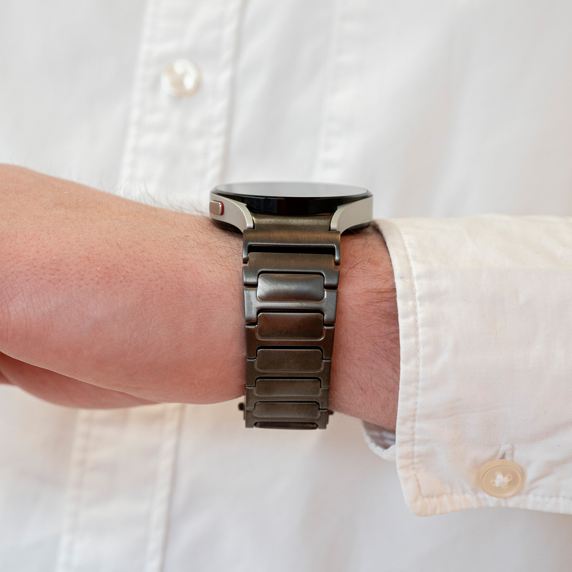 Nahaufnahme des Handgelenks eines Mannes mit einer dunklen Metall-Smartwatch und einem weißen Hemd.