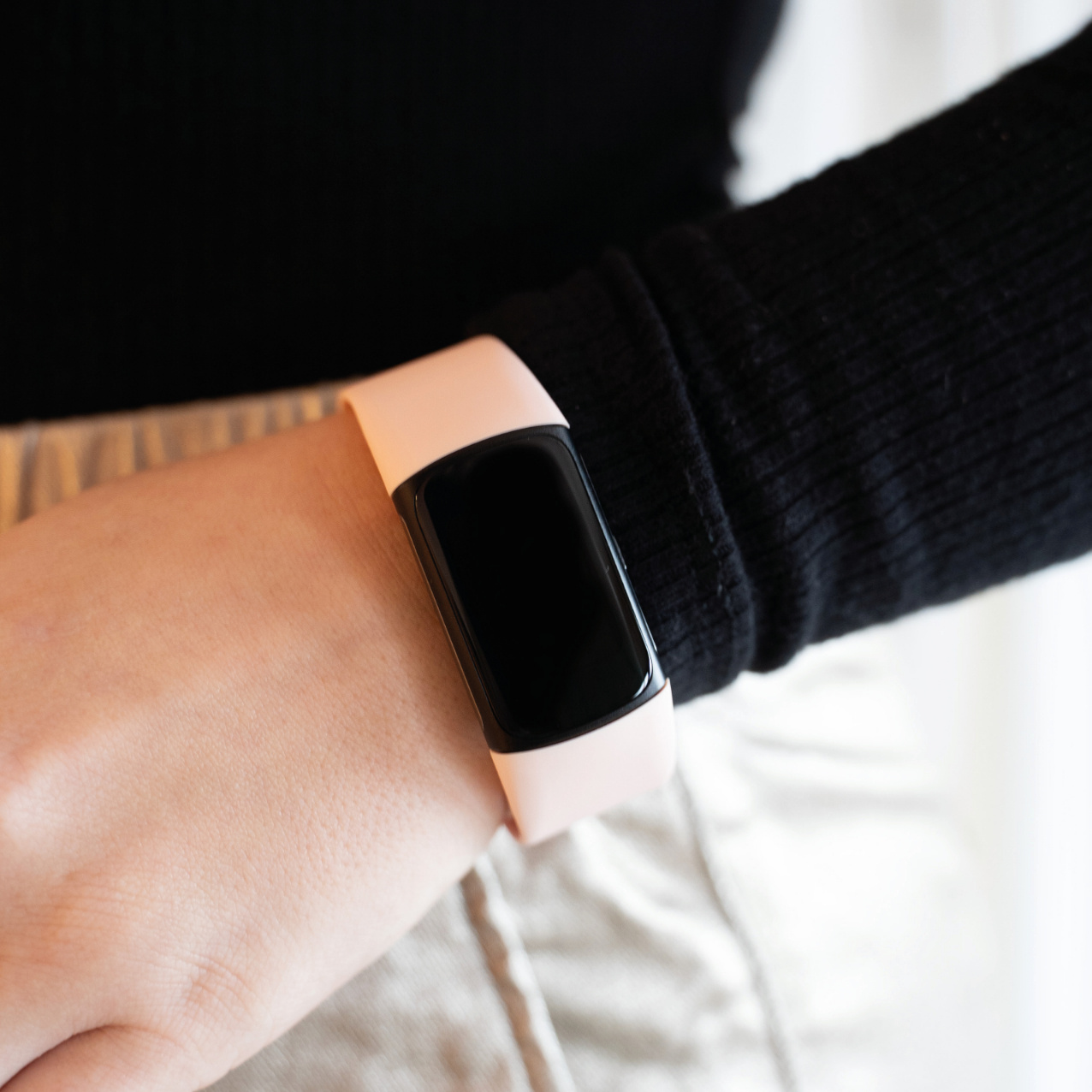 Das Handgelenk einer Person mit einer rosa Smartwatch. Das Handgelenk trägt einen schwarzen Ärmel.