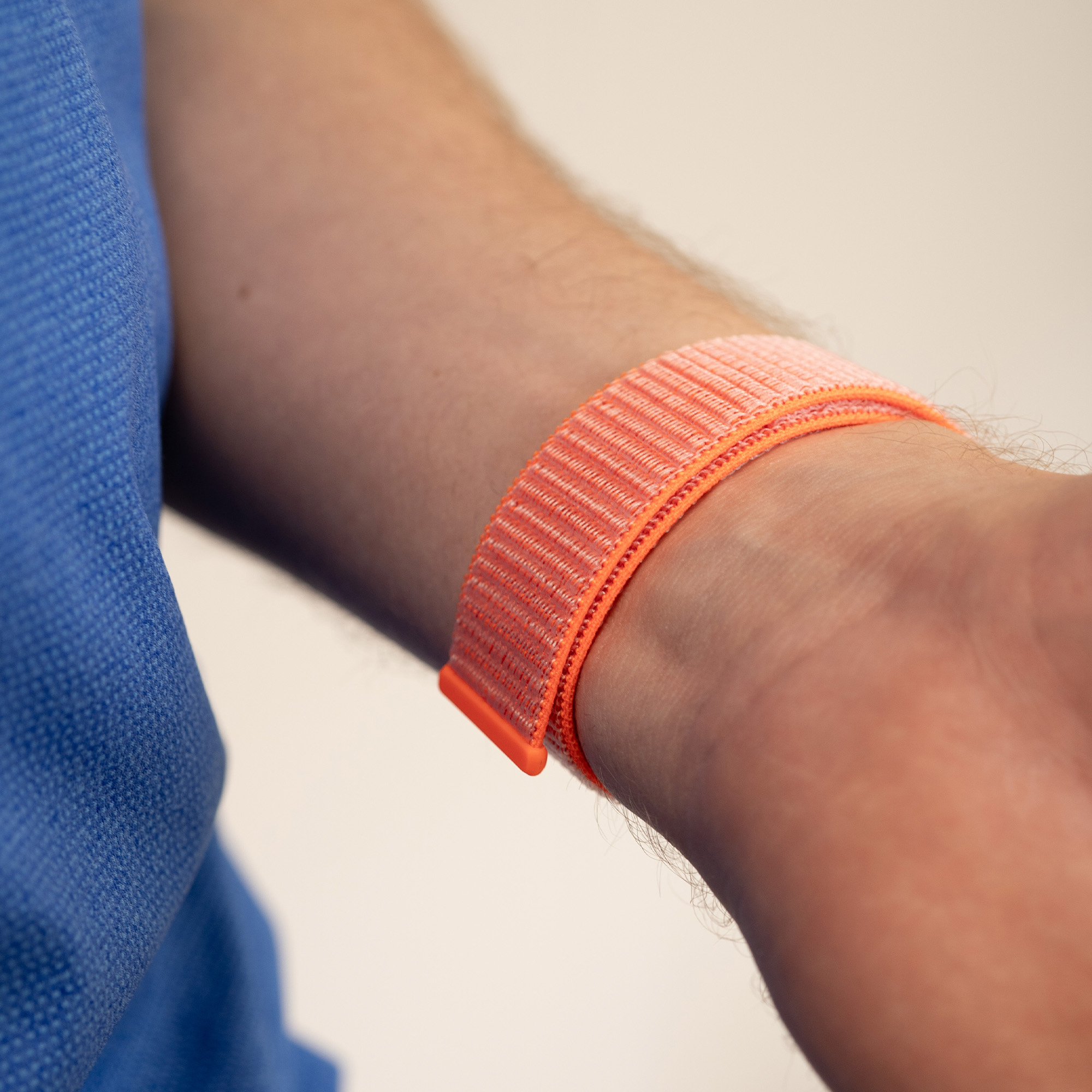 Das Handgelenk einer Person mit einem orangefarbenen Uhrenarmband vor einem blauen Hemdhintergrund.