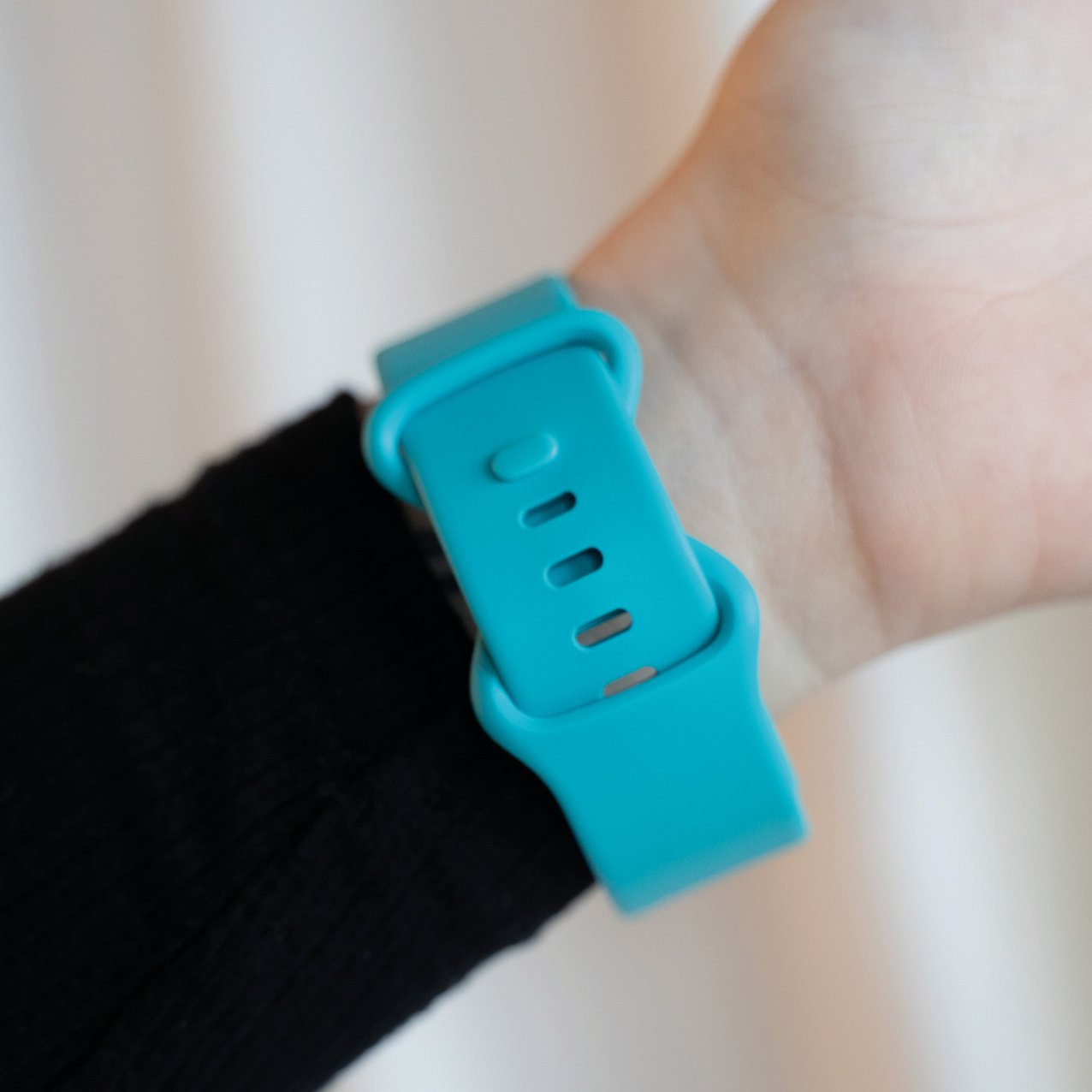 Ein Handgelenk mit einem türkisfarbenen Uhrenarmband. Das Band ist mit einem schwarzen Ärmel verbunden.