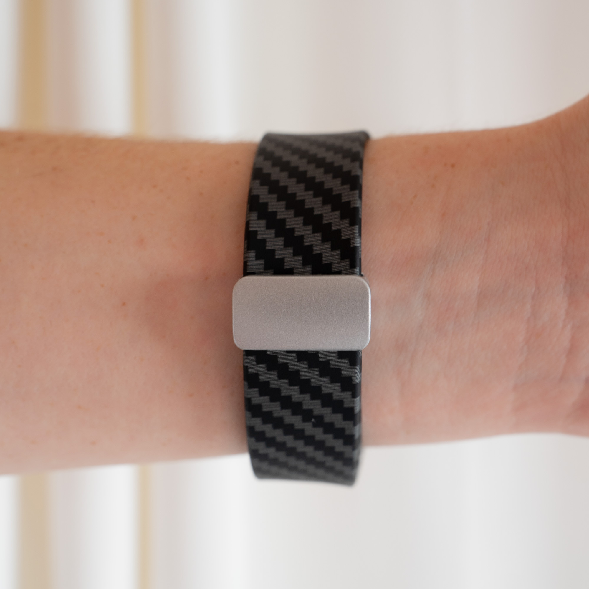 Ein Handgelenk mit einem schwarz-grauen Uhrenarmband. Das Uhrenarmband besteht aus Kohlefaser-Muster.