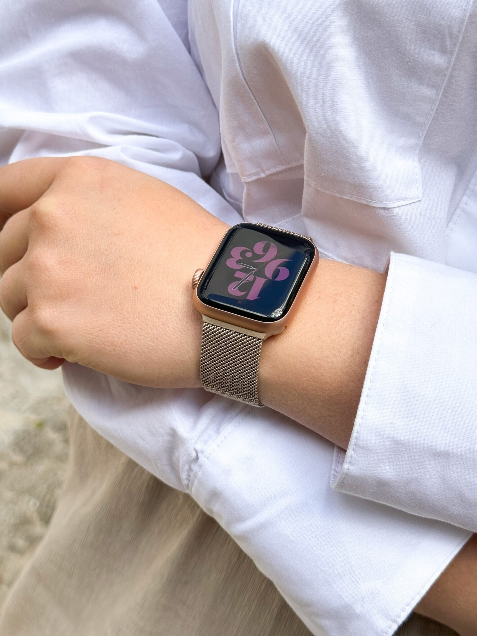 Ein Handgelenk mit goldener Smartwatch mit Mesh-Armband, trägt ein weißes Hemd.