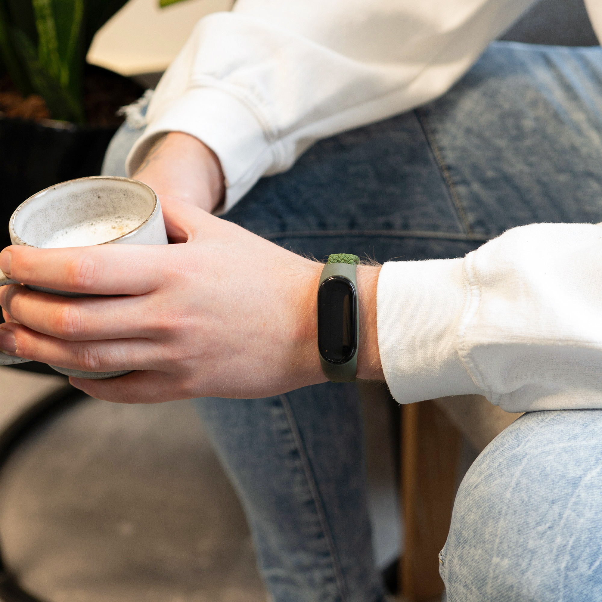 Person hält Kaffeetasse, trägt grünes Fitnessband. Band zeigt leeren schwarzen Bildschirm.