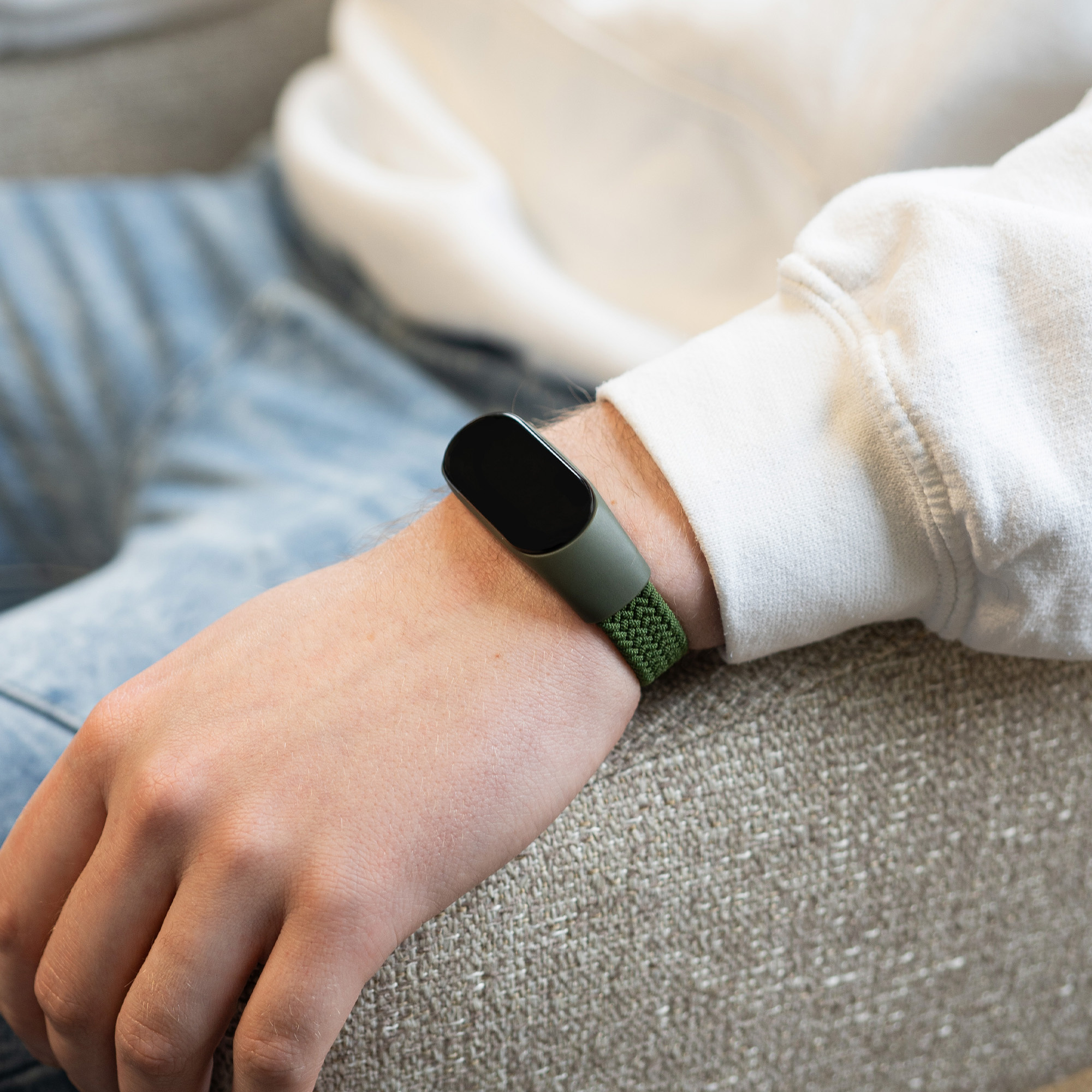 Ein Handgelenk mit einer grünen, geflochtenen Smartwatch am Handgelenk, mit Jeans.