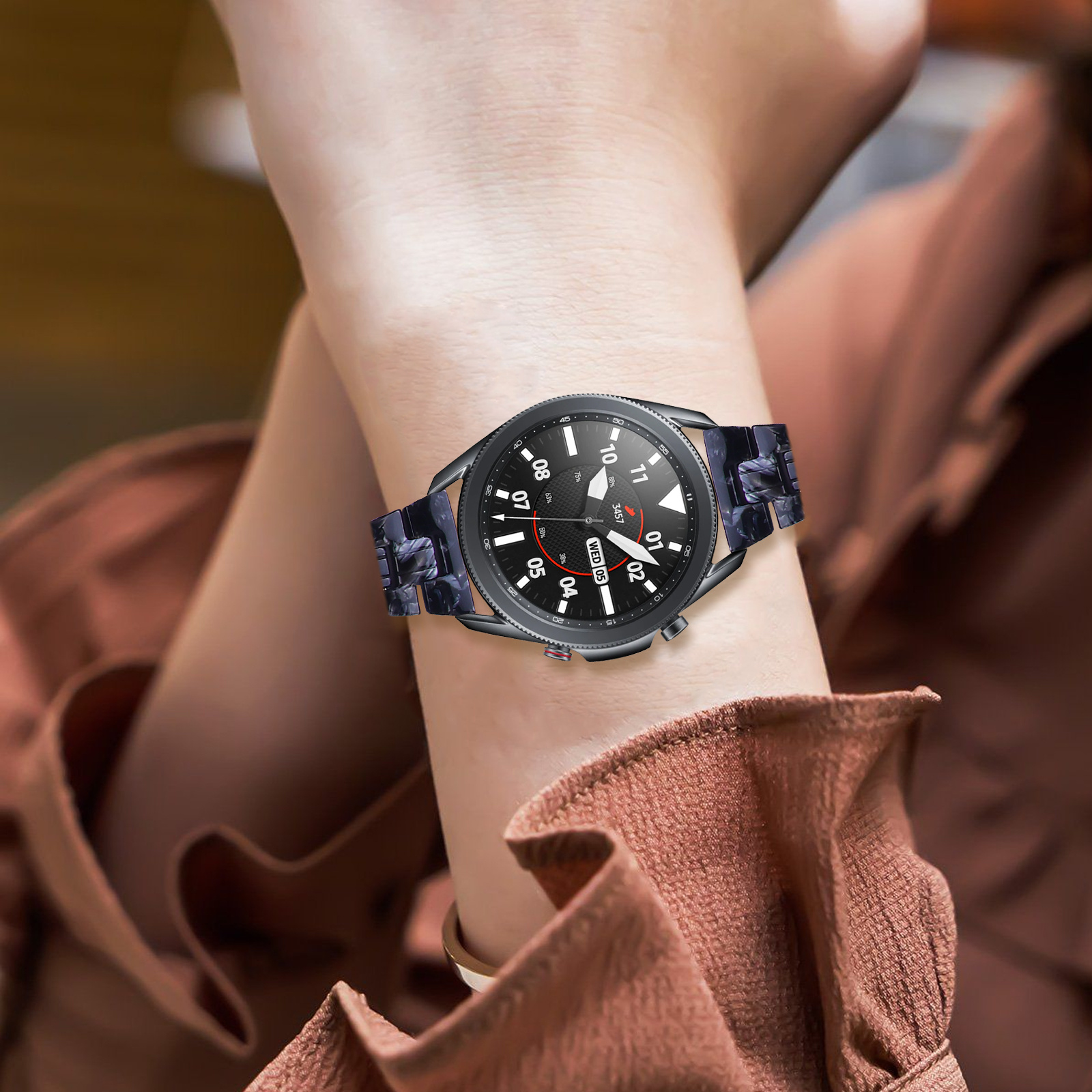 Das Handgelenk einer Person mit einer Uhr. Die Uhr hat ein schwarzes Zifferblatt und ein gemustertes Band.