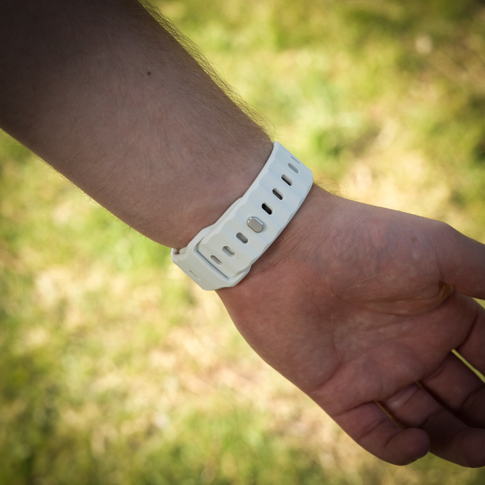Weißes Uhrenarmband an einem Handgelenk. Die Uhr ist schwarz. Die Person trägt ein blaues Hemd.