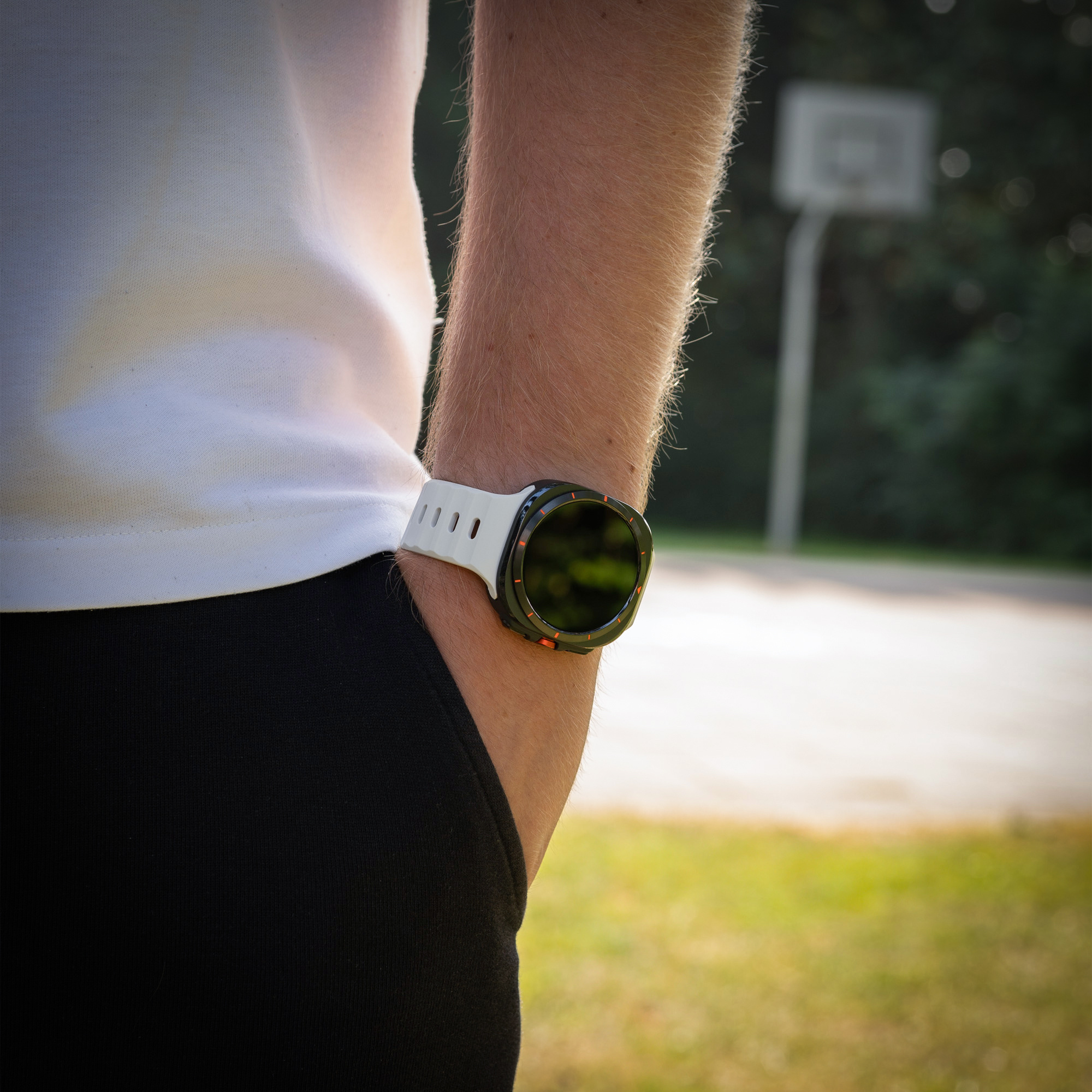 Handgelenk mit schwarz-weißer Uhr. Schwarze Shorts und Basketballplatz im Hintergrund.