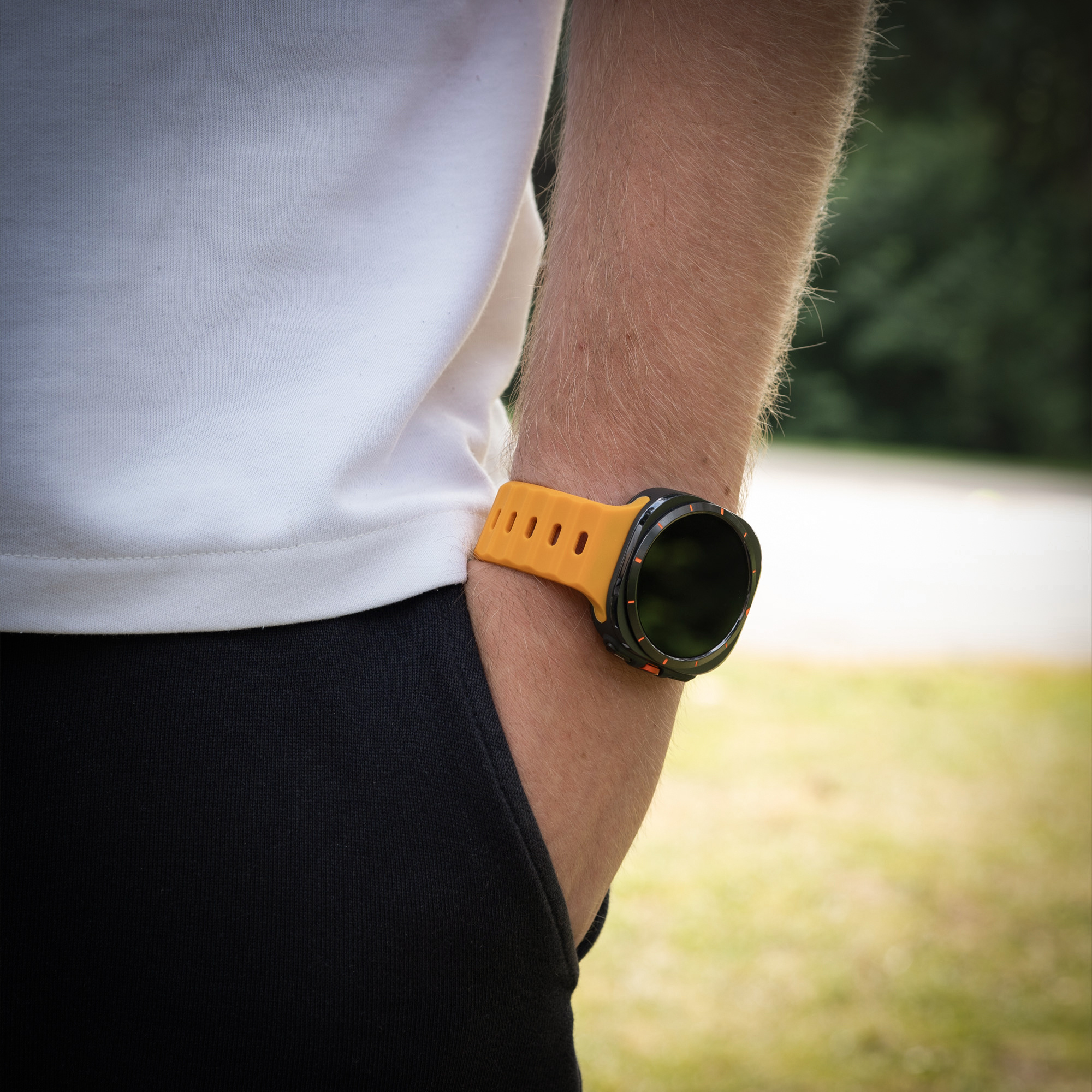 Ein Arm einer Person mit einer orangefarbenen Uhr. Sie tragen ein weißes Hemd und eine schwarze Hose.