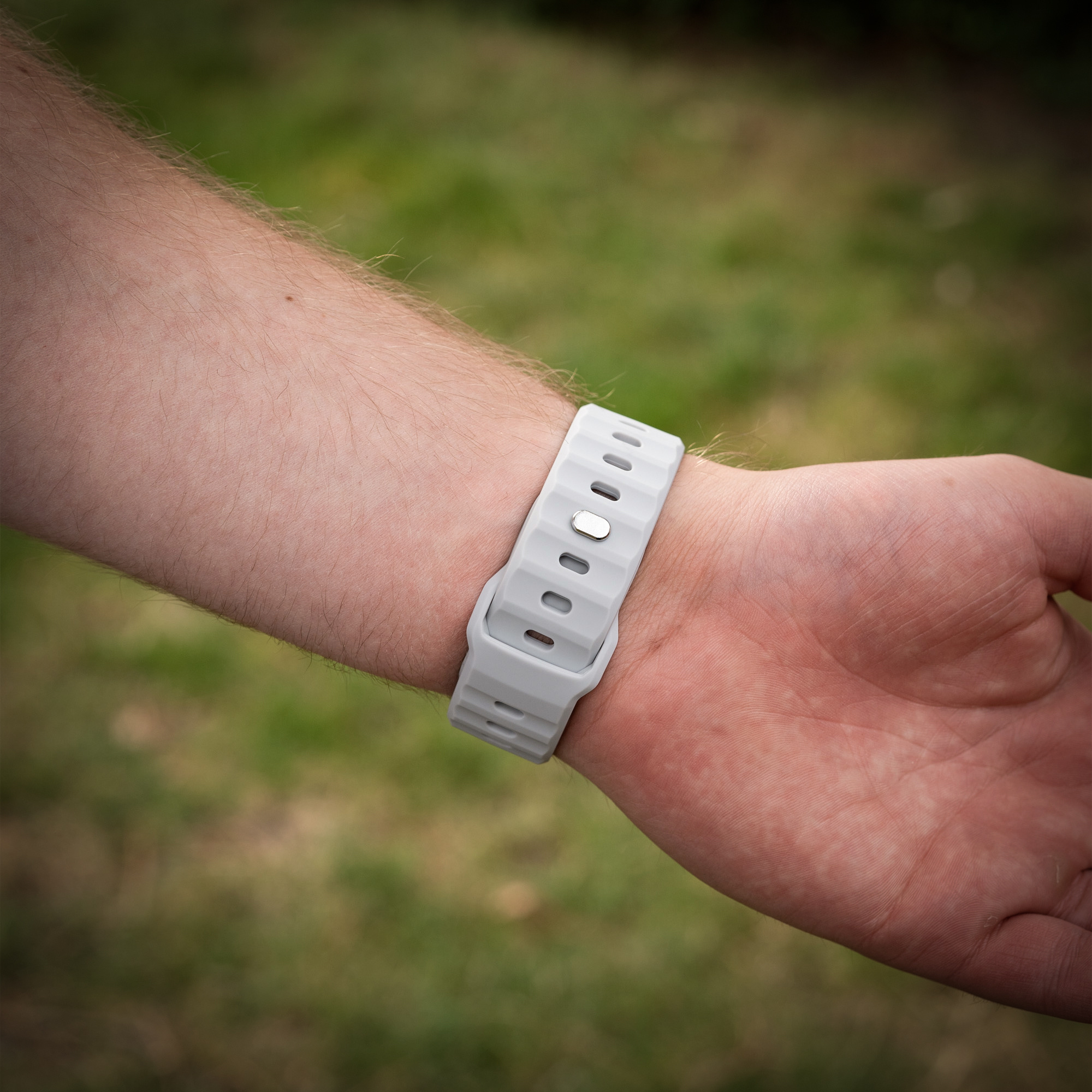 Handgelenk einer Person mit grauem Uhrenarmband. Das Band ist geschnallt und auf grünem Hintergrund.
