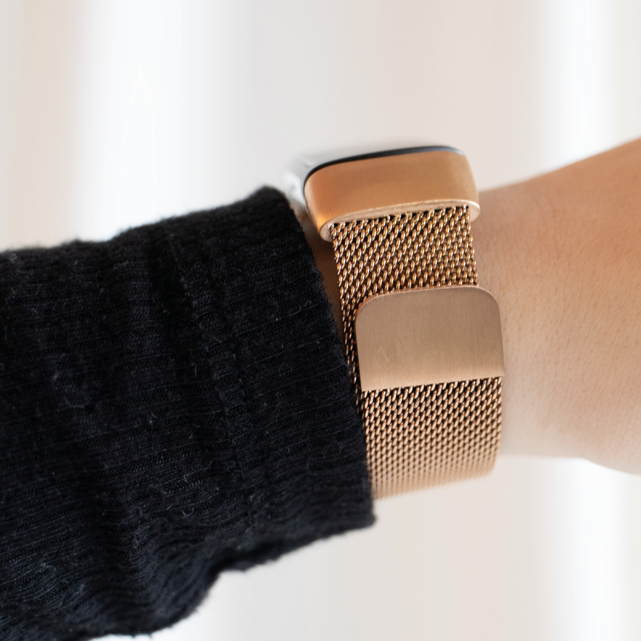 Das Handgelenk einer Person mit einem roségoldenen Mesh-Uhrenarmband, Nahaufnahme, vor einem schwarzen Pullover.