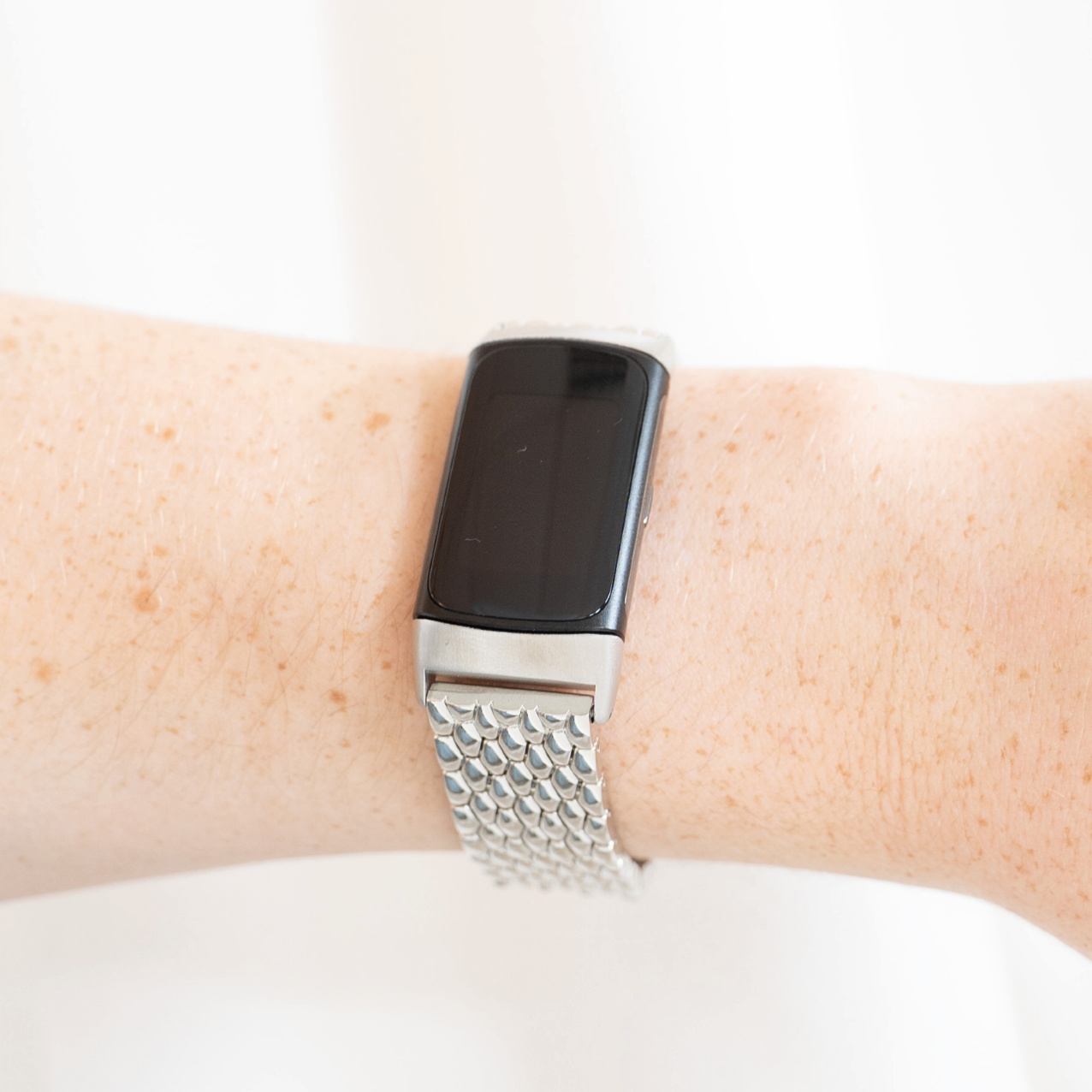 Eine Person trägt eine silberne Smartwatch mit einem verbundenen Metallarmband. Die Uhr ist an ihrem Handgelenk.