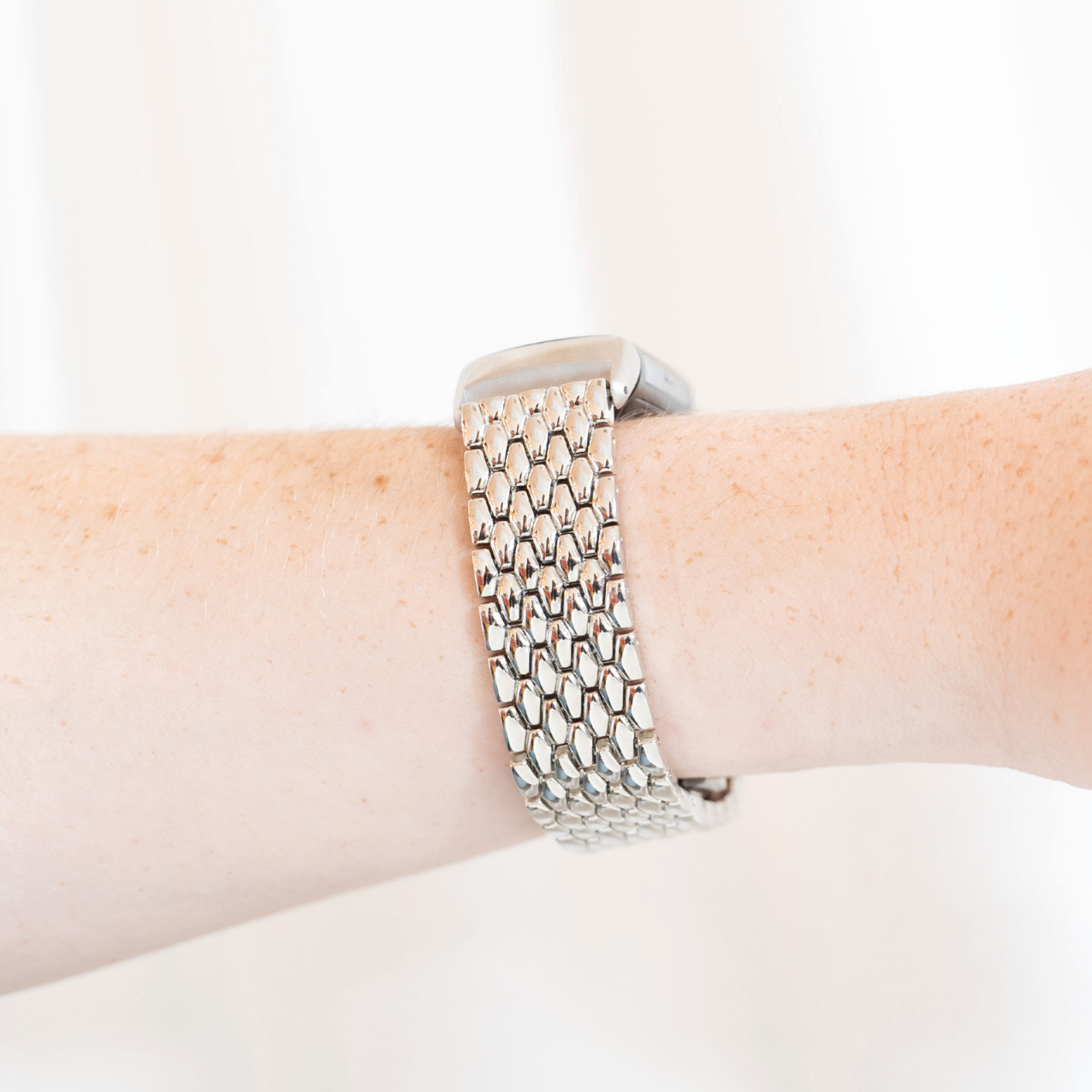 Handgelenk mit einer silbernen Smartwatch und einem kettenartigen silbernen Armband. Weißer Hintergrund.