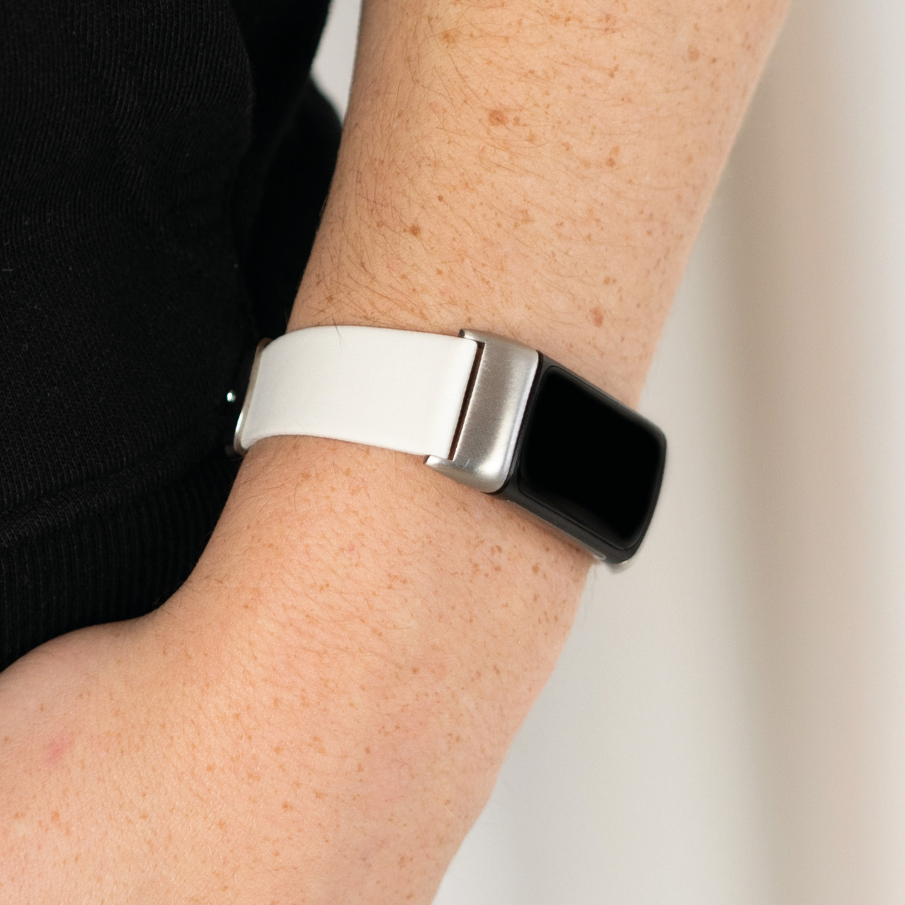 Arm einer Person mit weißer und schwarzer Uhr, Nahaufnahme. Weißer Hintergrund, trägt eine Uhr.