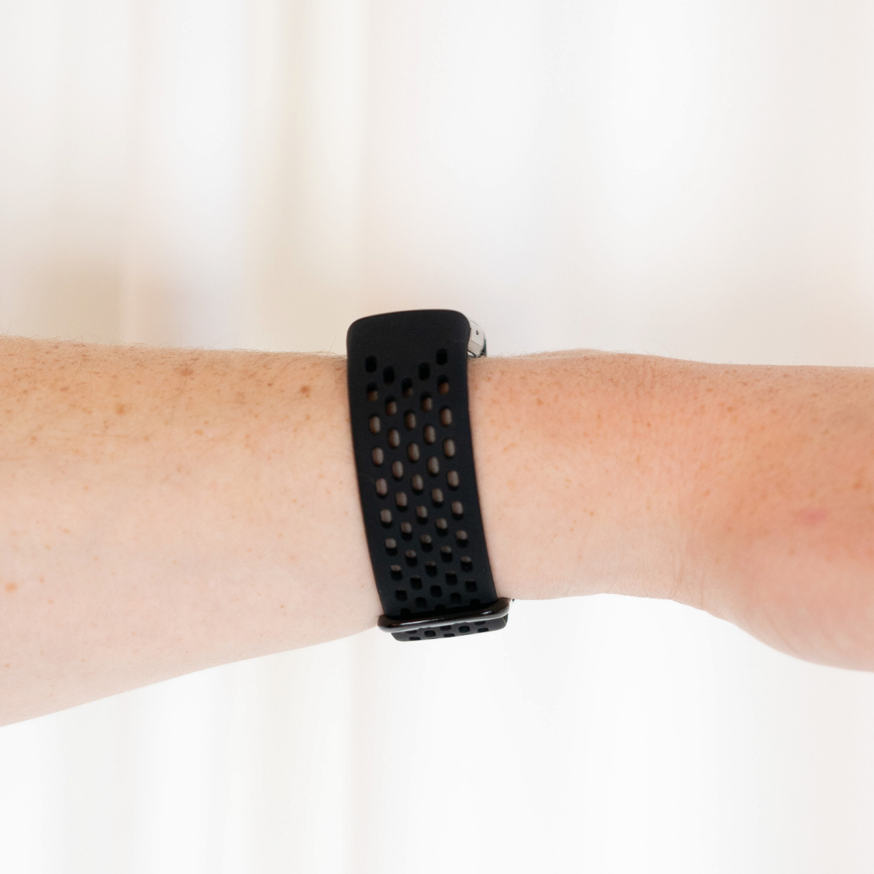 Schwarzes Armband mit Löchern. Arm mit Sommersprossen. Weißer Hintergrund. Sportliches Design.