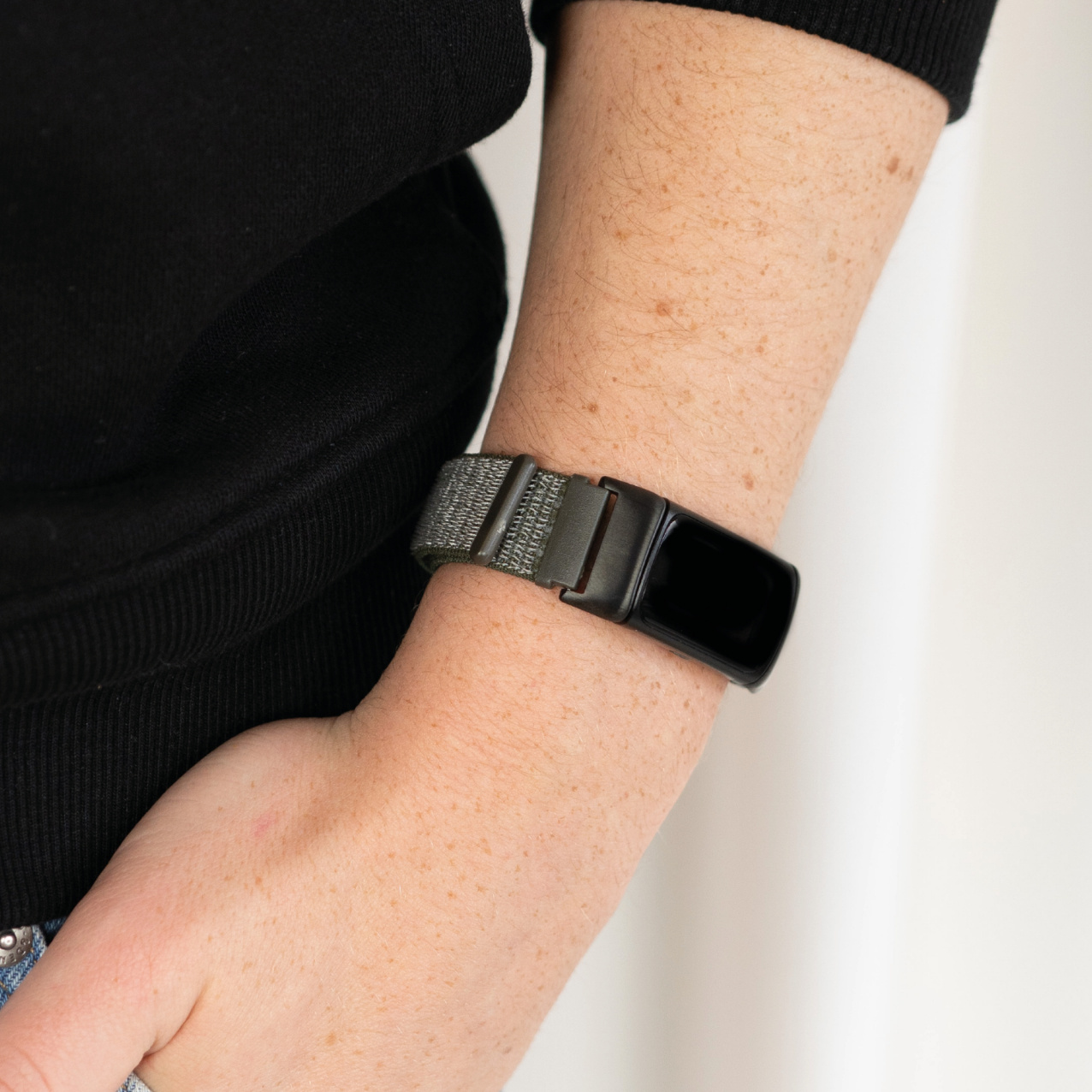 Eine Person trägt einen grauen und schwarzen Fitnesstracker am Handgelenk. Das Band ist befestigt.
