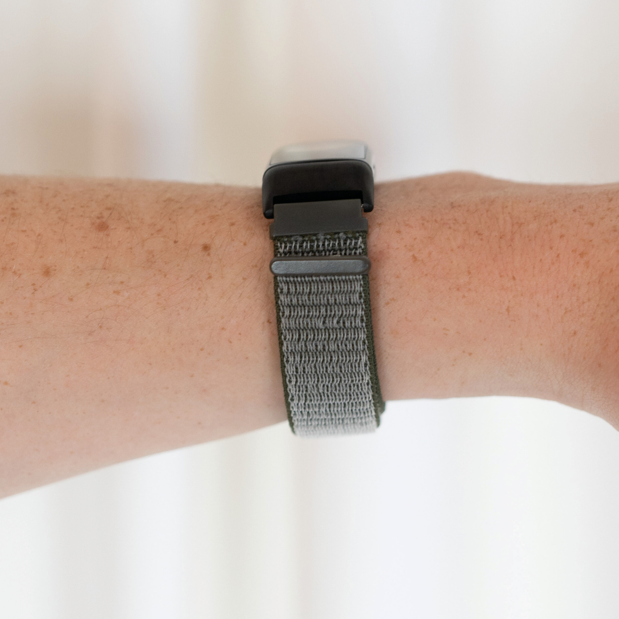 Handgelenk mit grün-grauem Uhrenarmband.