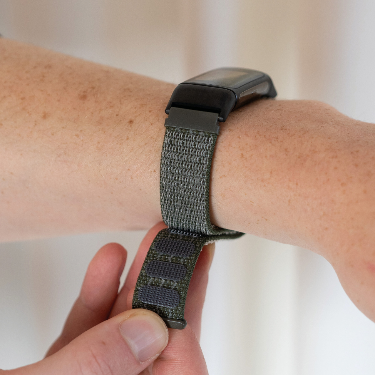 Die Hand einer Person befestigt ein grünes gewebtes Uhrenarmband an ihrem Handgelenk.