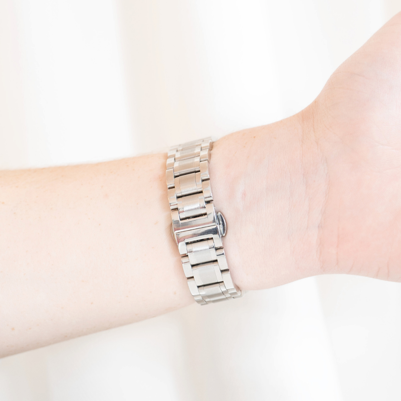 Eine silberne Uhr ist an einem Handgelenk. Das Band ist ineinander verschlungen.
