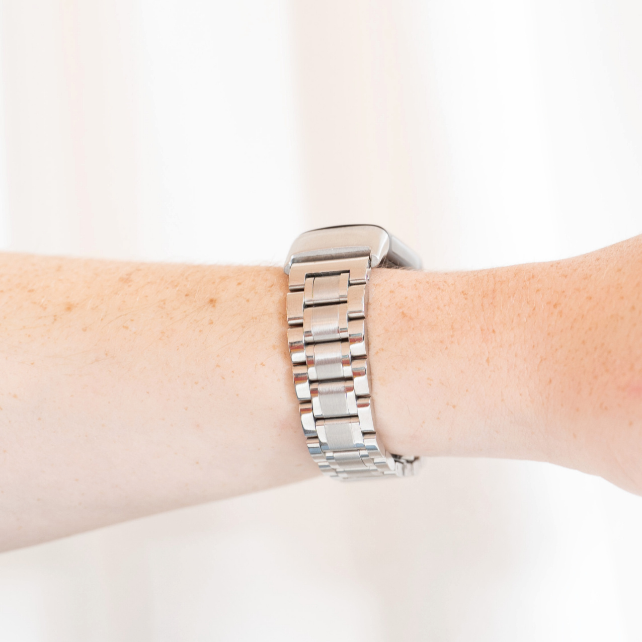 Eine silberne Smartwatch mit Metallarmband befindet sich an einem sommersprossigen Handgelenk und zeigt die Seite.