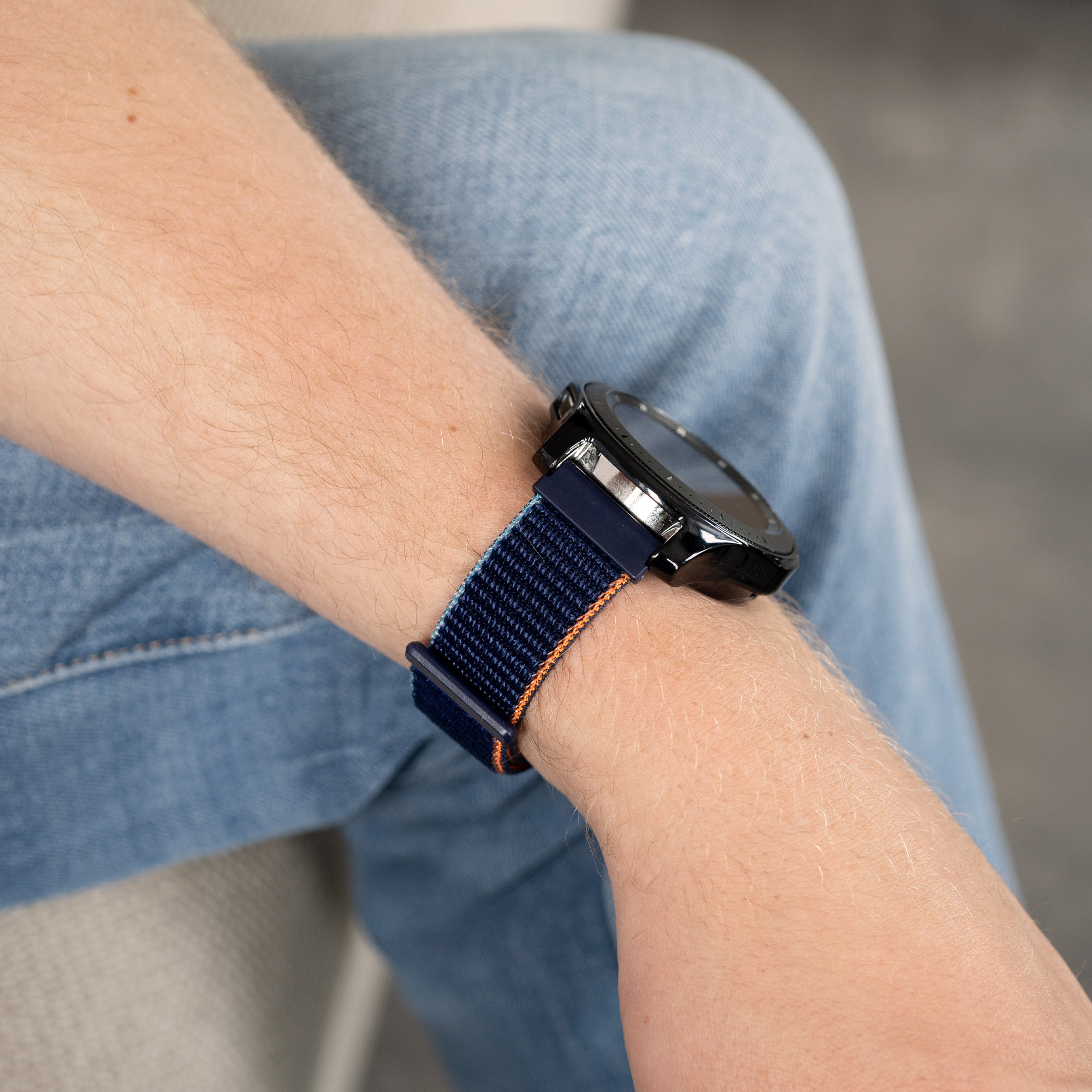 Handgelenk einer Person mit Uhr. Blaues und oranges Armband.