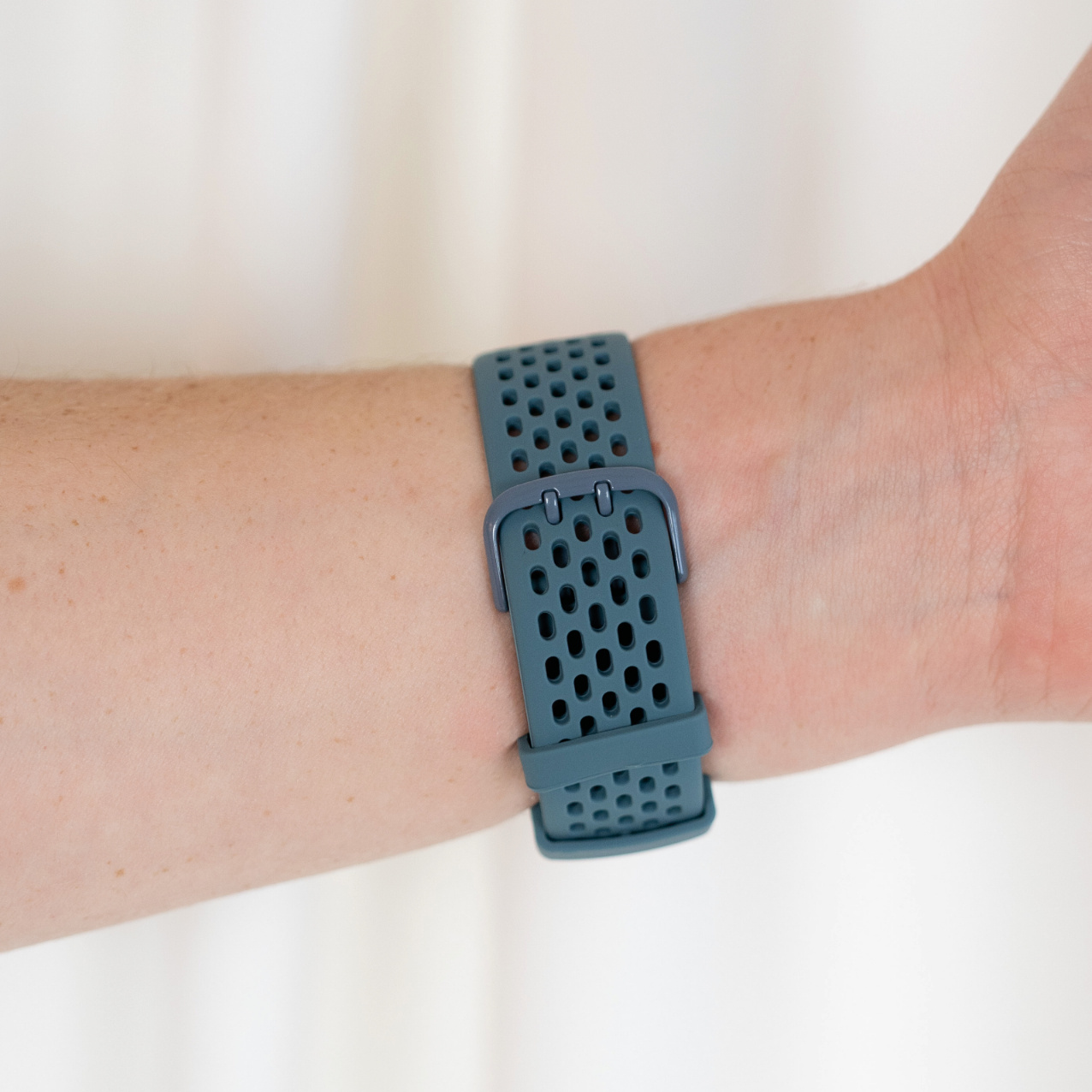 Ein türkisfarbenes Uhrenarmband ist am Handgelenk befestigt. Das Armband hat viele kleine Löcher.