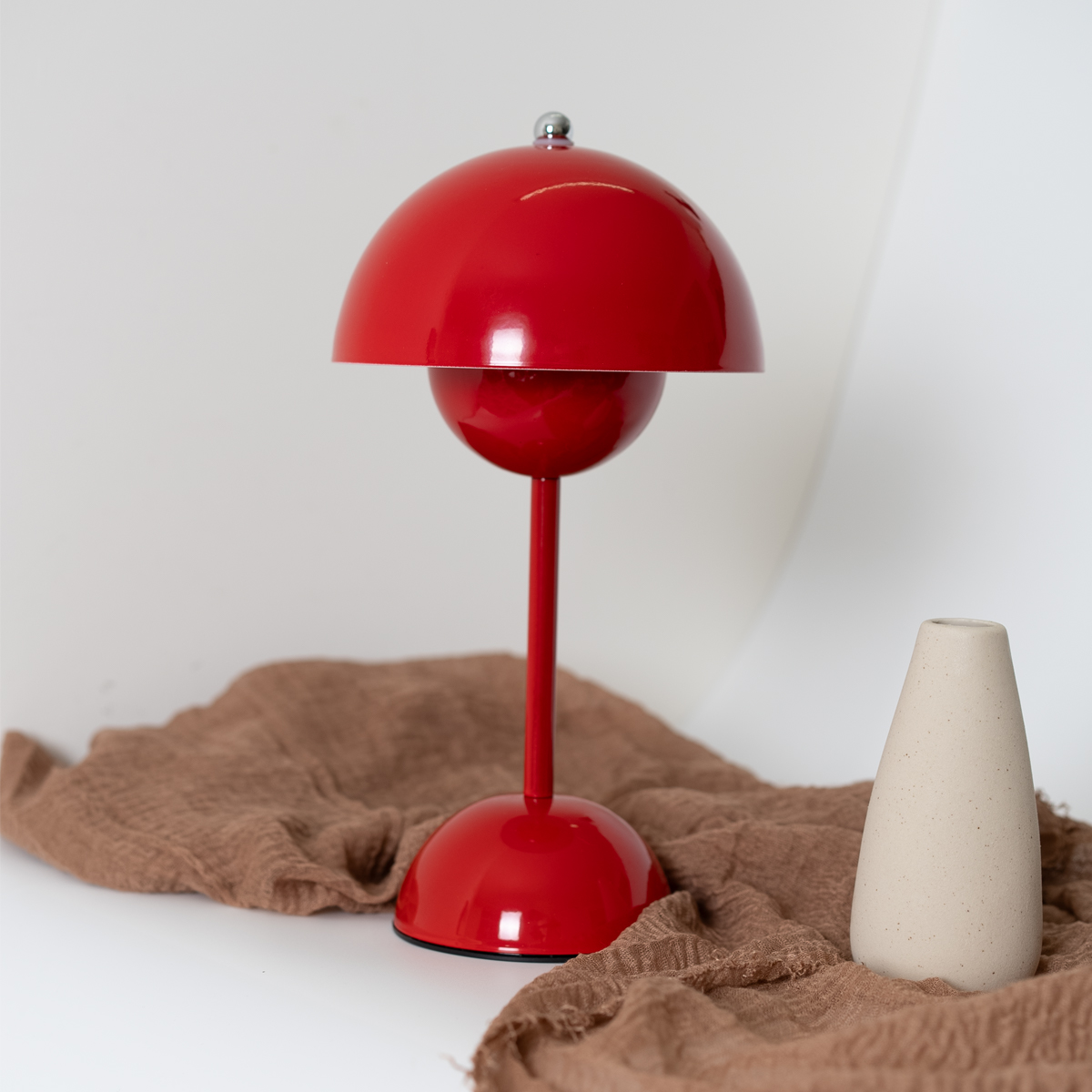 Lámpara de mesa roja con pantalla roja, con fondo blanco y un jarrón.
