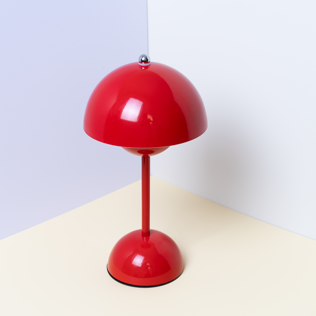 Una lámpara de mesa roja con base y pantalla redondas. Sobre superficie amarilla.