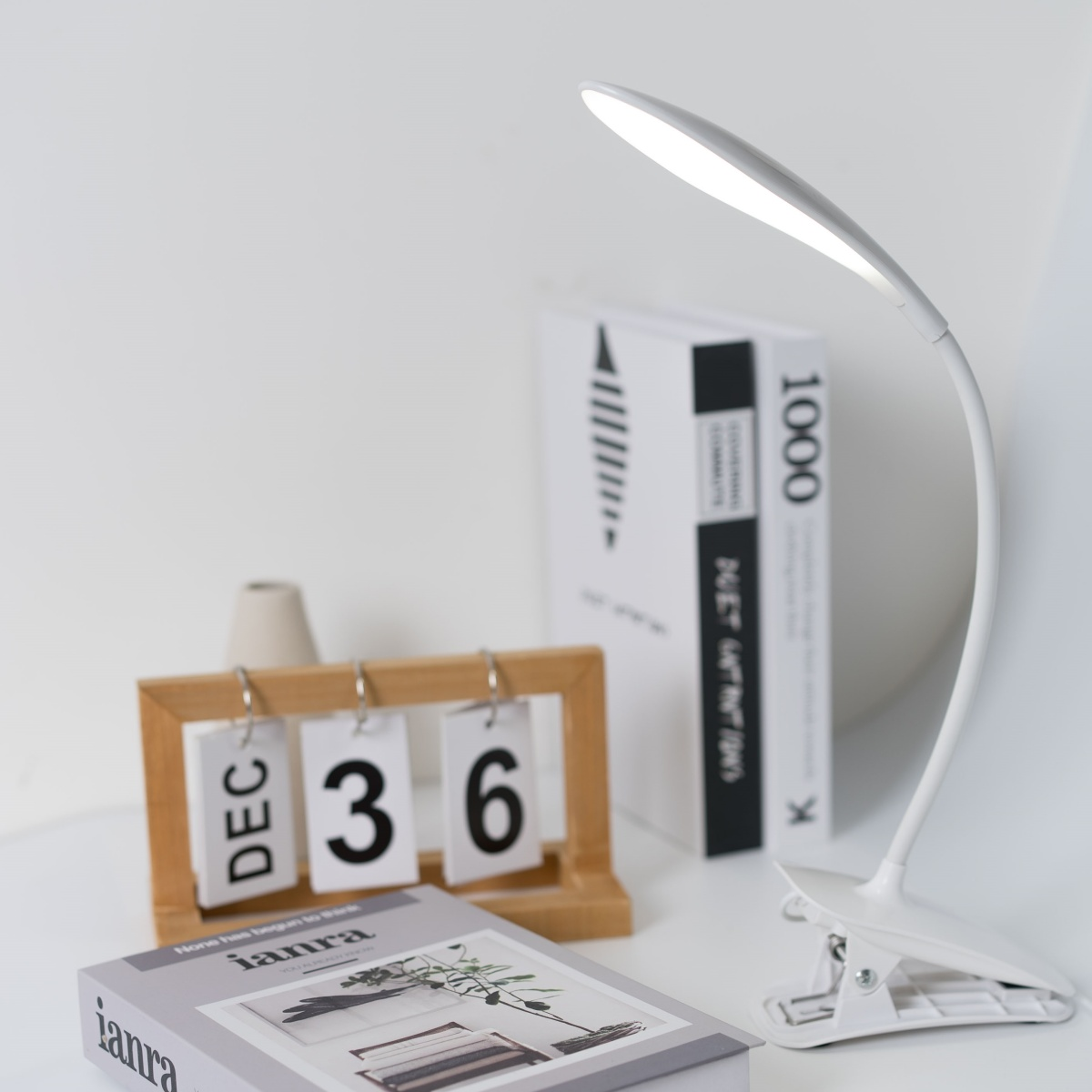 Una lámpara de escritorio blanca y curvada que ilumina un escritorio con un calendario y libros.