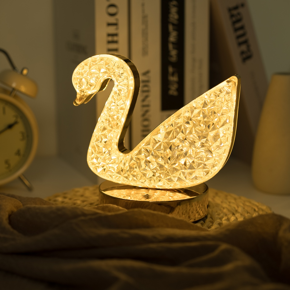 Lámpara en forma de cisne con base dorada, libros y un reloj en el fondo.