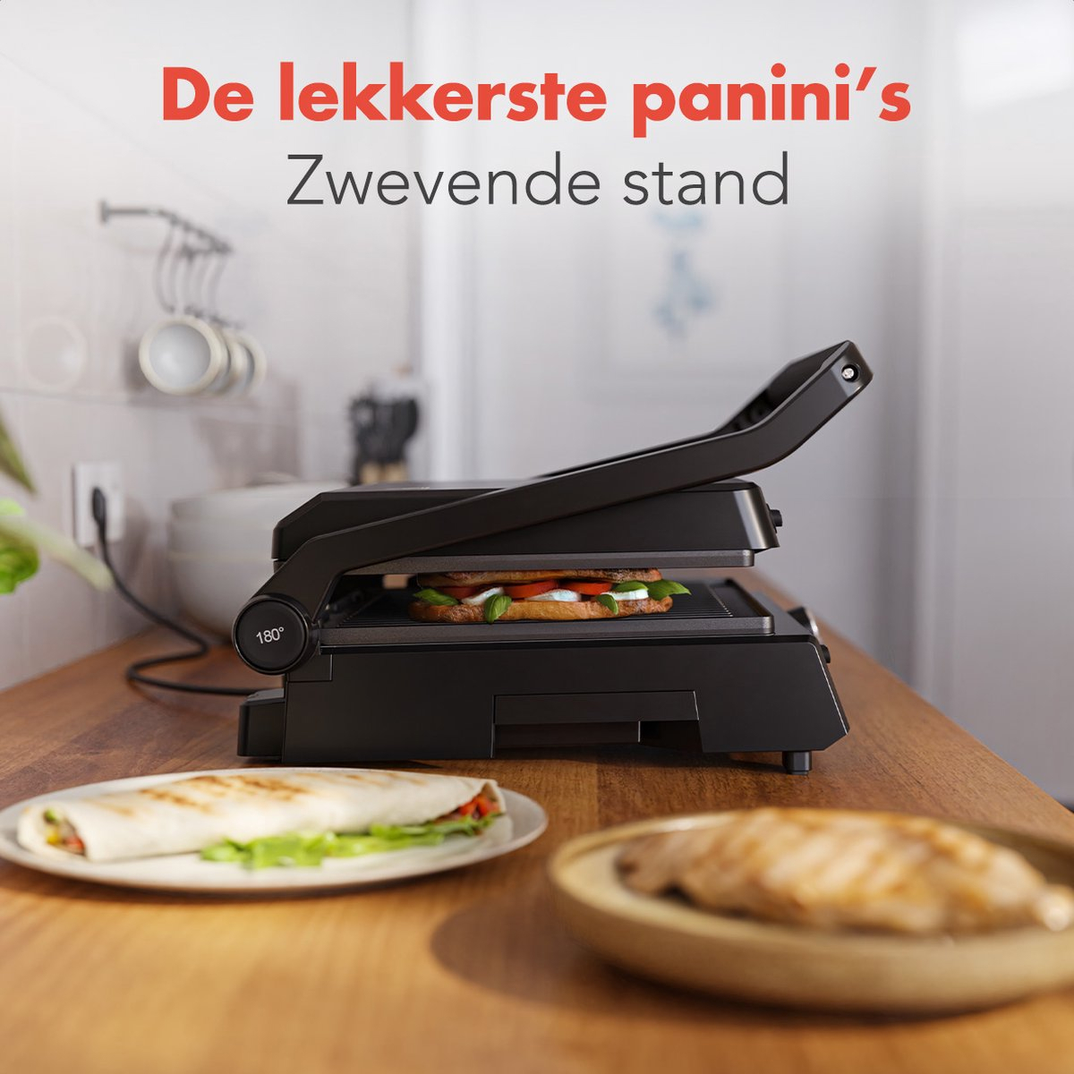 A black panini press with food inside, on a wooden surface. There is a wrap and a plate.