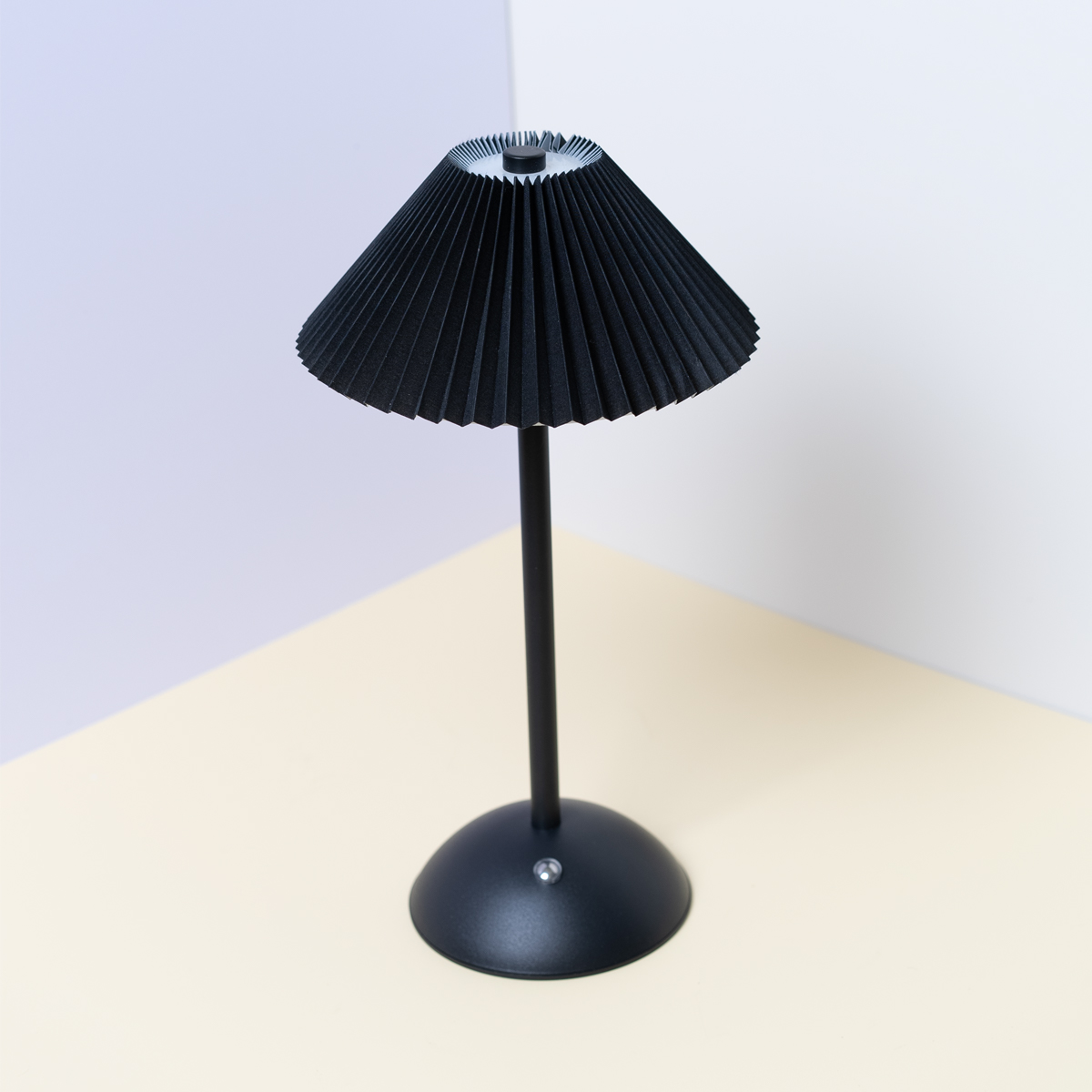 Una lámpara de mesa negra con una pantalla plisada y una base negra, sobre una superficie beige.