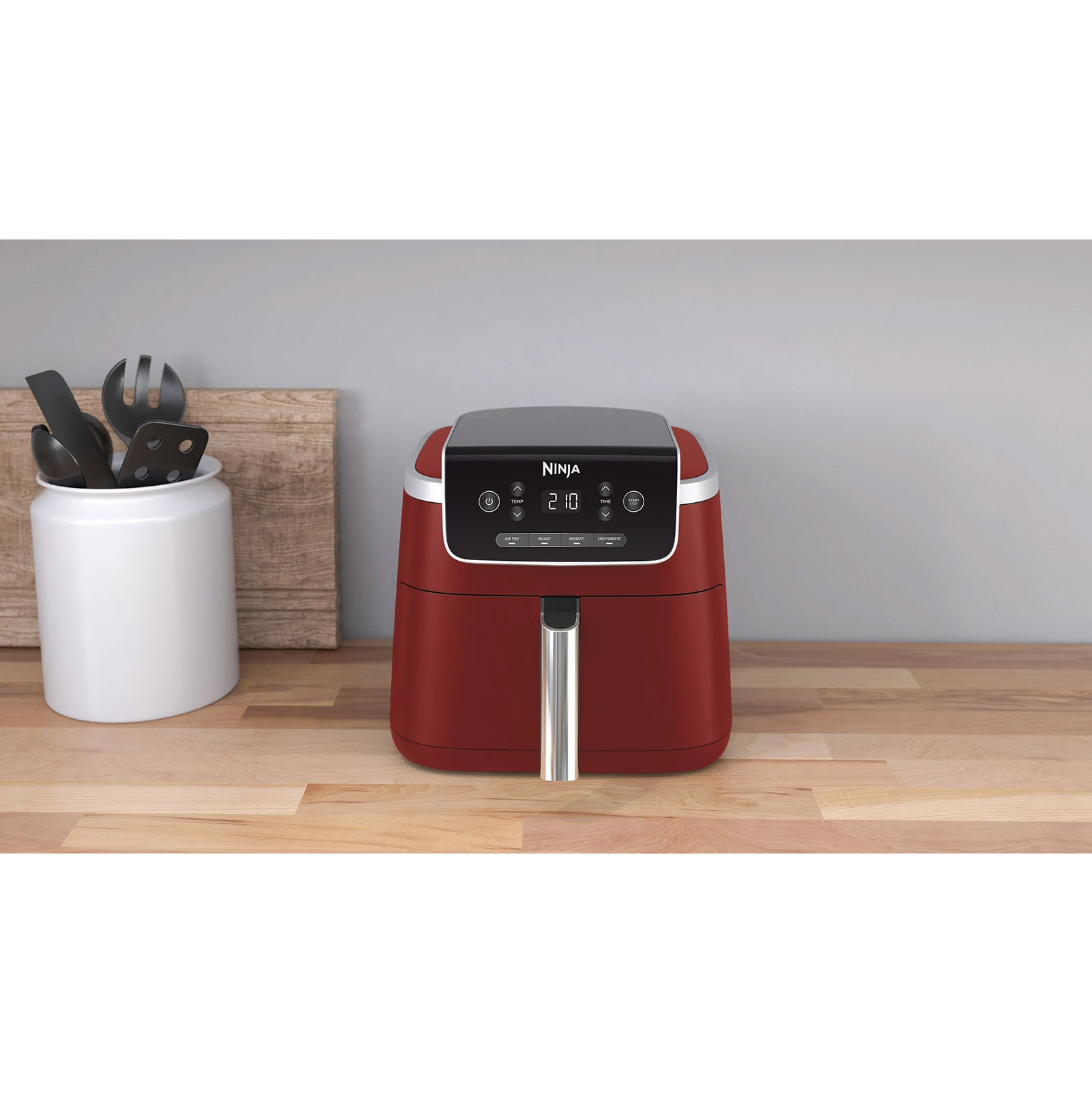 Czerwona frytownica na drewnianym blacie. Ma cyfrowy wyświetlacz i uchwyt. Szare tło.