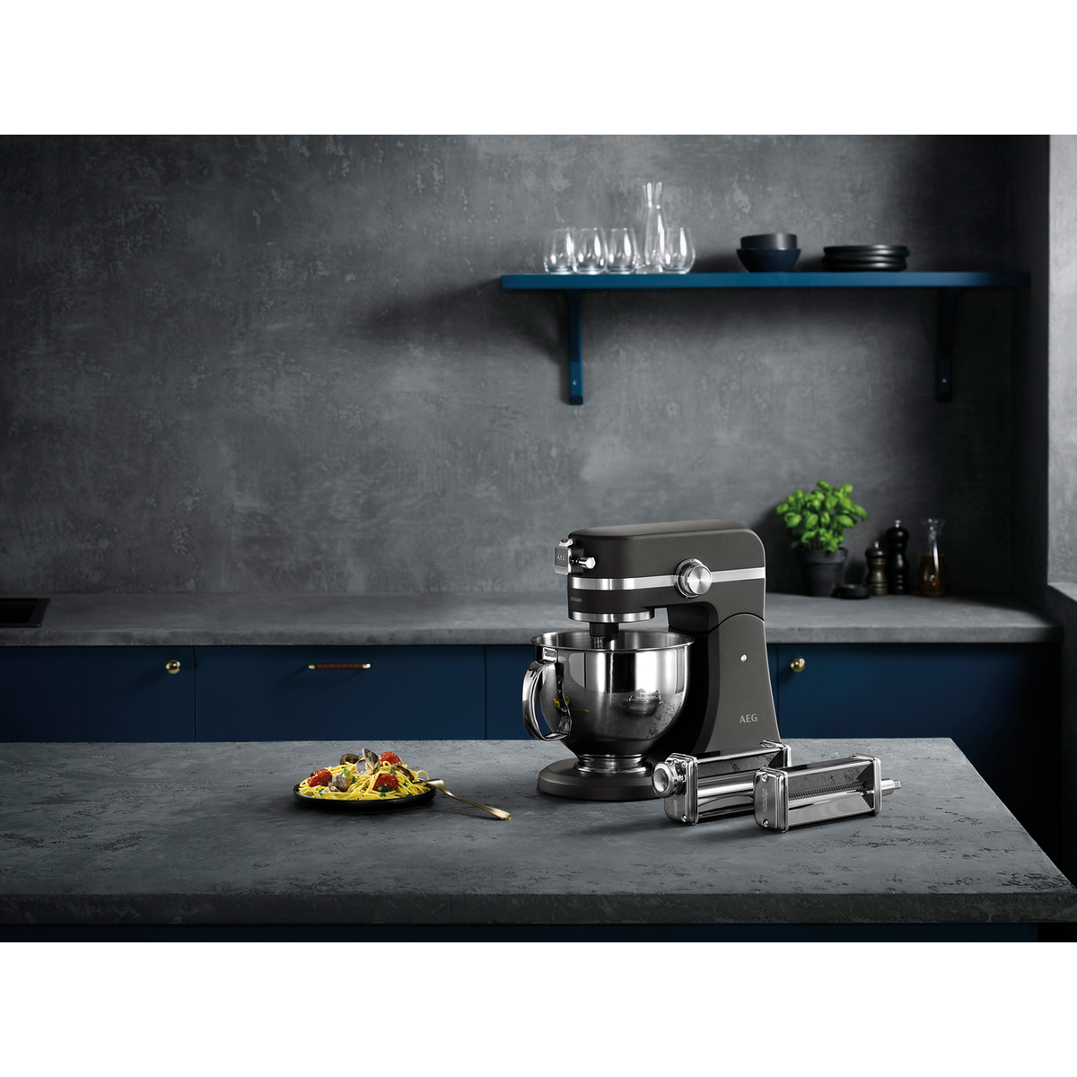 Una batidora de cocina negra con accesorios para hacer pasta en una encimera con comida y otros elementos.