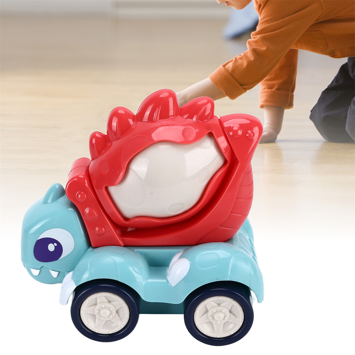 Ein blaues und rotes Spielzeugauto in Form eines Dinosauriers. Die Hand eines Kindes greift danach.