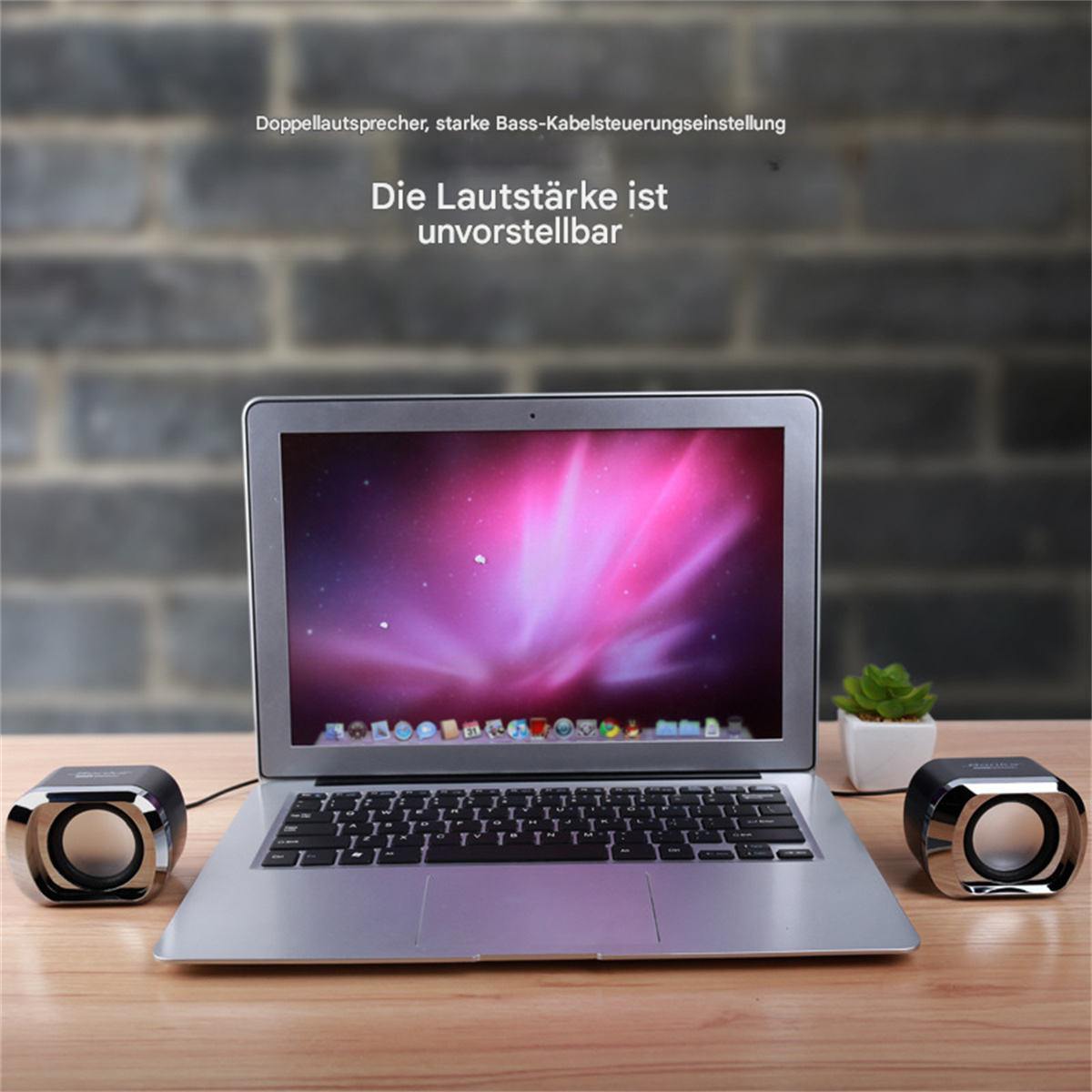 Laptop auf einem Holztisch mit Lautsprechern. Der Bildschirm zeigt Text, Hintergrund Backsteinmauer.