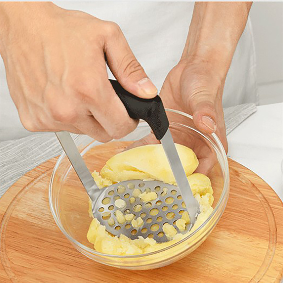 Hände zerdrücken Kartoffeln in einer Glasschüssel mit einem Kartoffelstampfer.