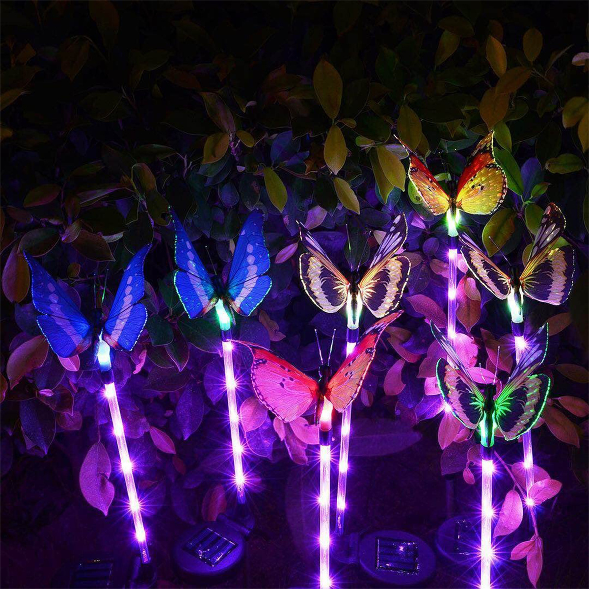 Schmetterlinge auf Stäben, beleuchtet mit lila Licht. Schmetterlinge haben verschiedene Farben und Muster, in einem Garten.