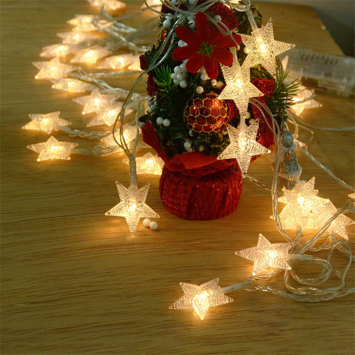 Weihnachtsbeleuchtung mit sternförmigen Lichtern auf einem Holztisch. Ein kleiner Baum hinten.