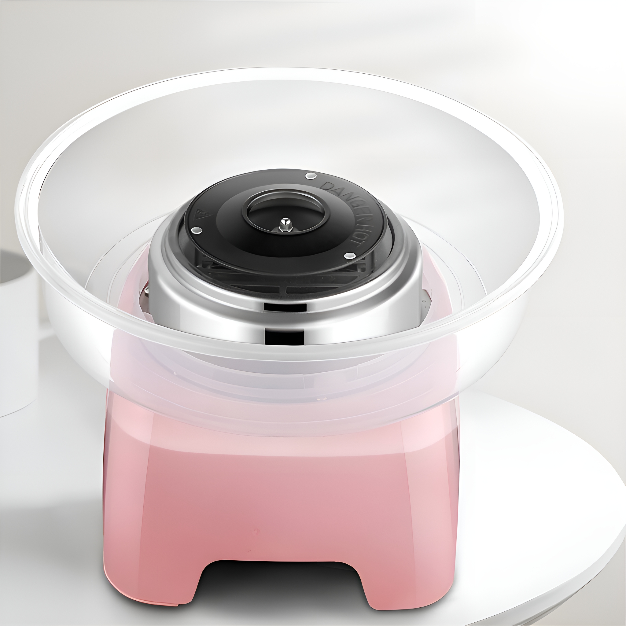 Eine rosa Zuckerwattemaschine mit einer durchsichtigen Schüssel auf einem weißen Tisch.