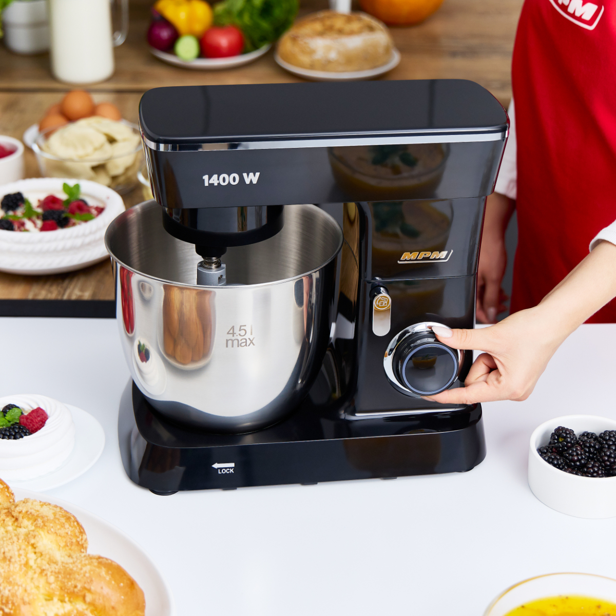 La mano di una persona che regola la manopola di un mixer da cucina nero. Altri oggetti da cucina sullo sfondo.