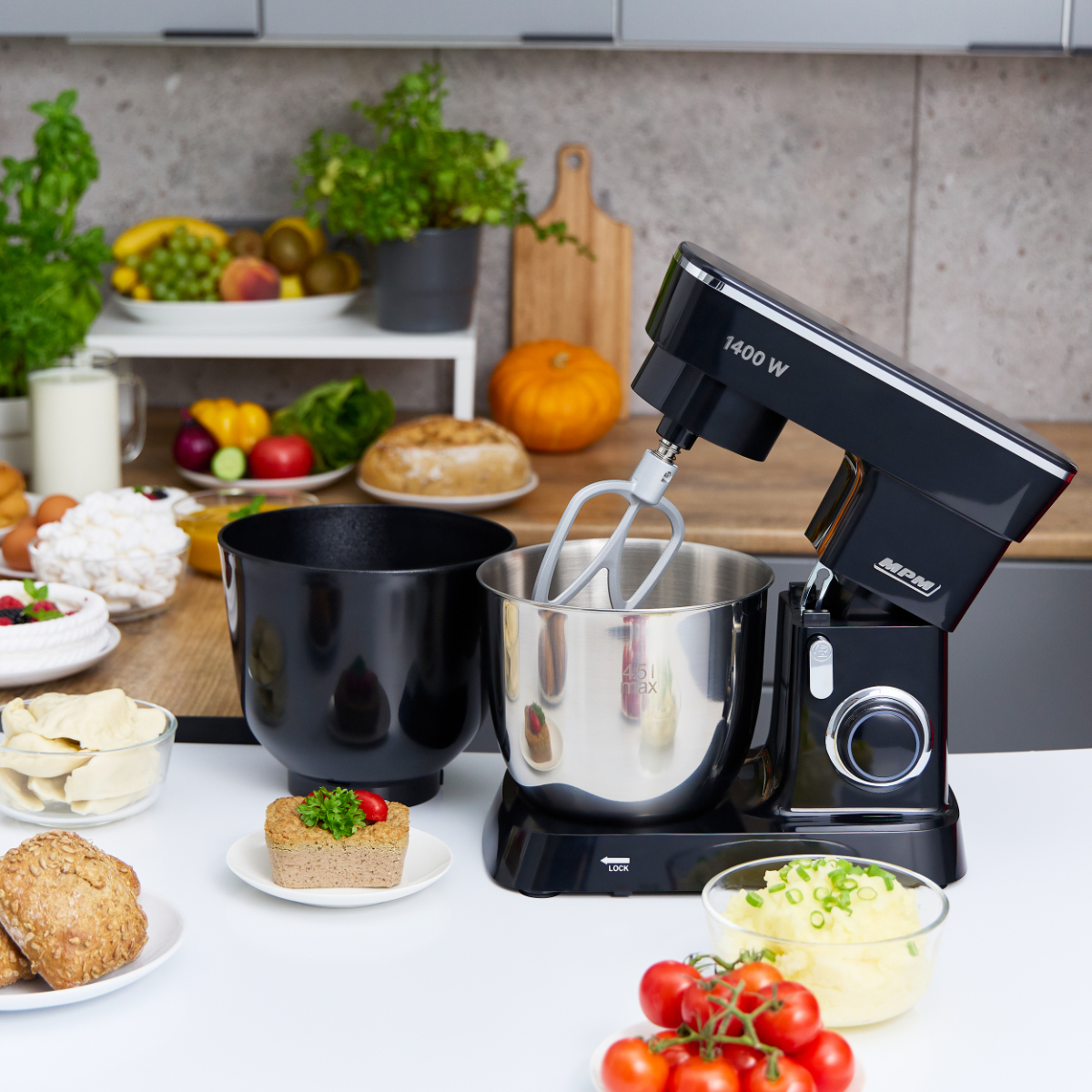 Robot da cucina nero e argento con ciotole e generi alimentari su un bancone bianco e sfondo grigio.