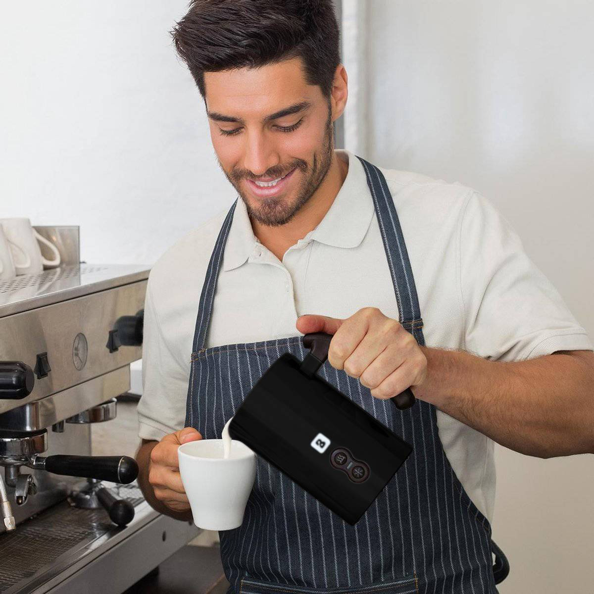 Ein Barista gießt Milch aus einem schwarzen Aufschäumer in eine weiße Tasse.