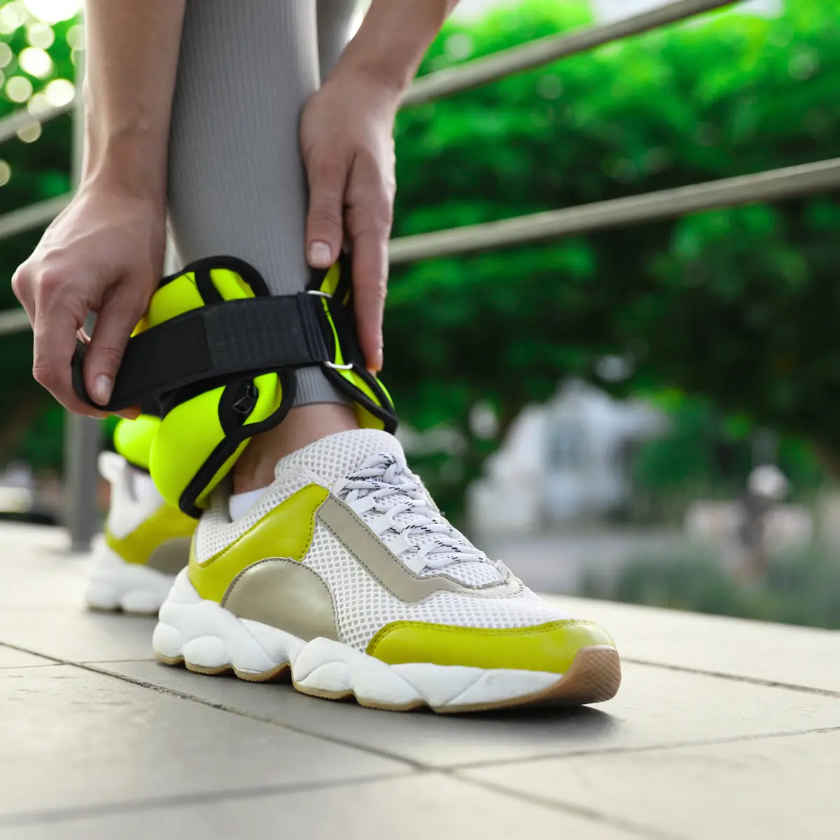 A person putting on ankle weights. They wear sneakers and leggings, in an outdoor setting.