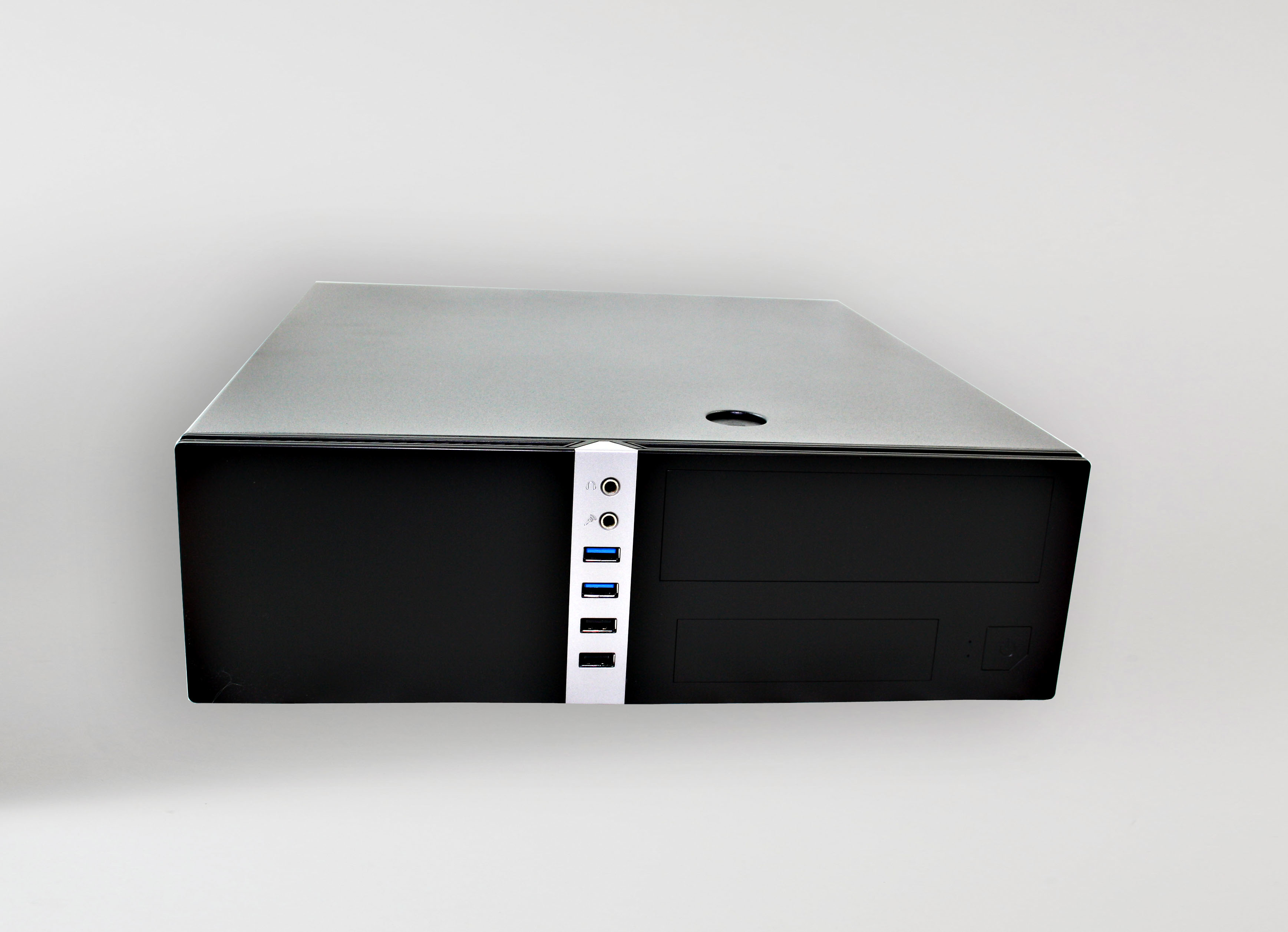 Czarna obudowa komputera z białym panelem przednim. Tło to jasnoszara powierzchnia.