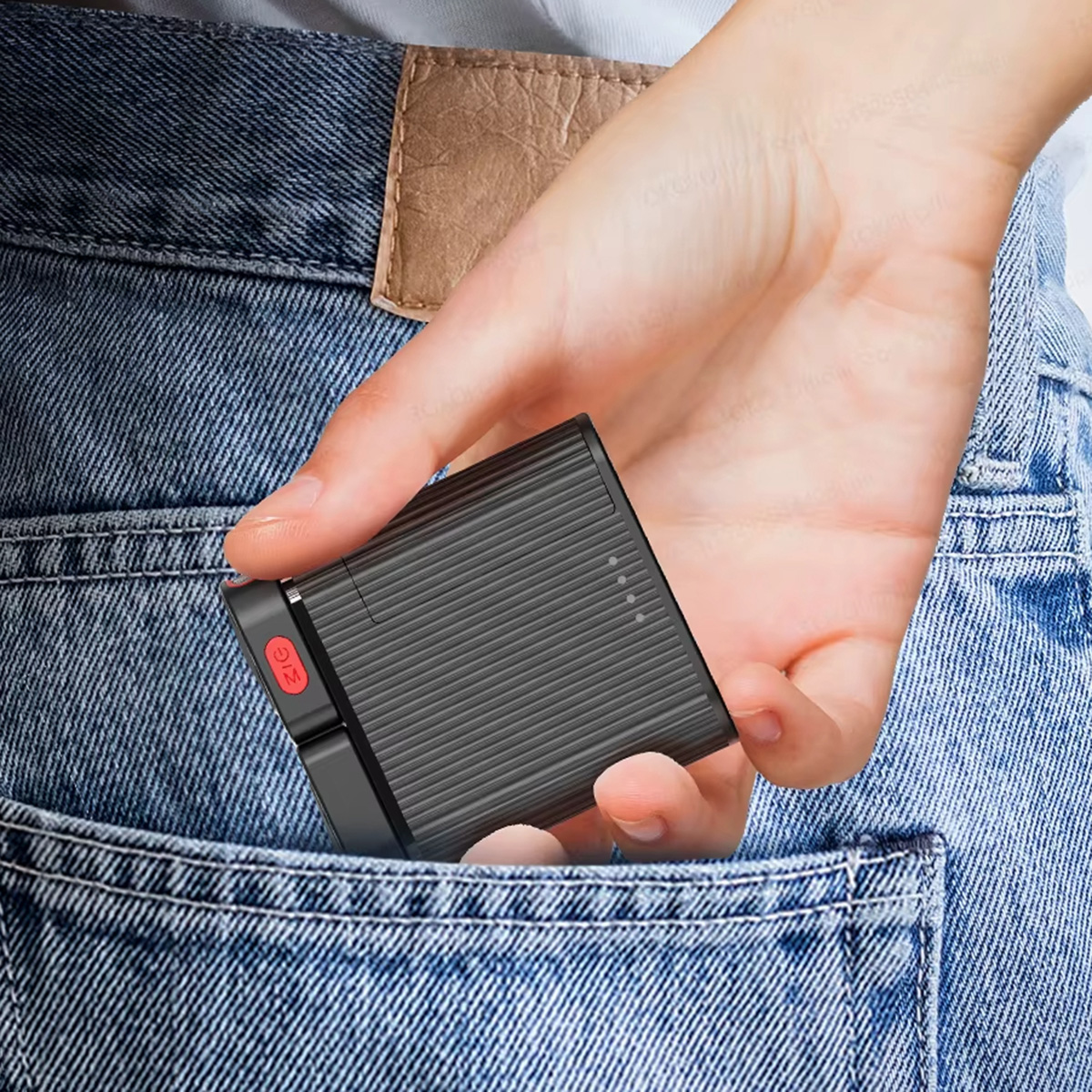Un pequeño dispositivo negro con un botón rojo en el bolsillo de un jean, vista parcial de la mano.